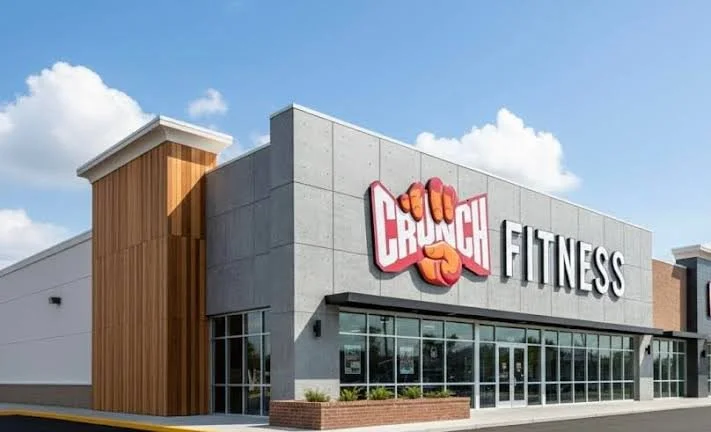 Exterior view of a Crunch Fitness gym with a large sign featuring a clenched fist logo on the front of the building.
