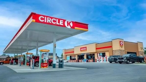 Circle K gas station with fueling pumps, convenience store, and parked cars under a blue sky.