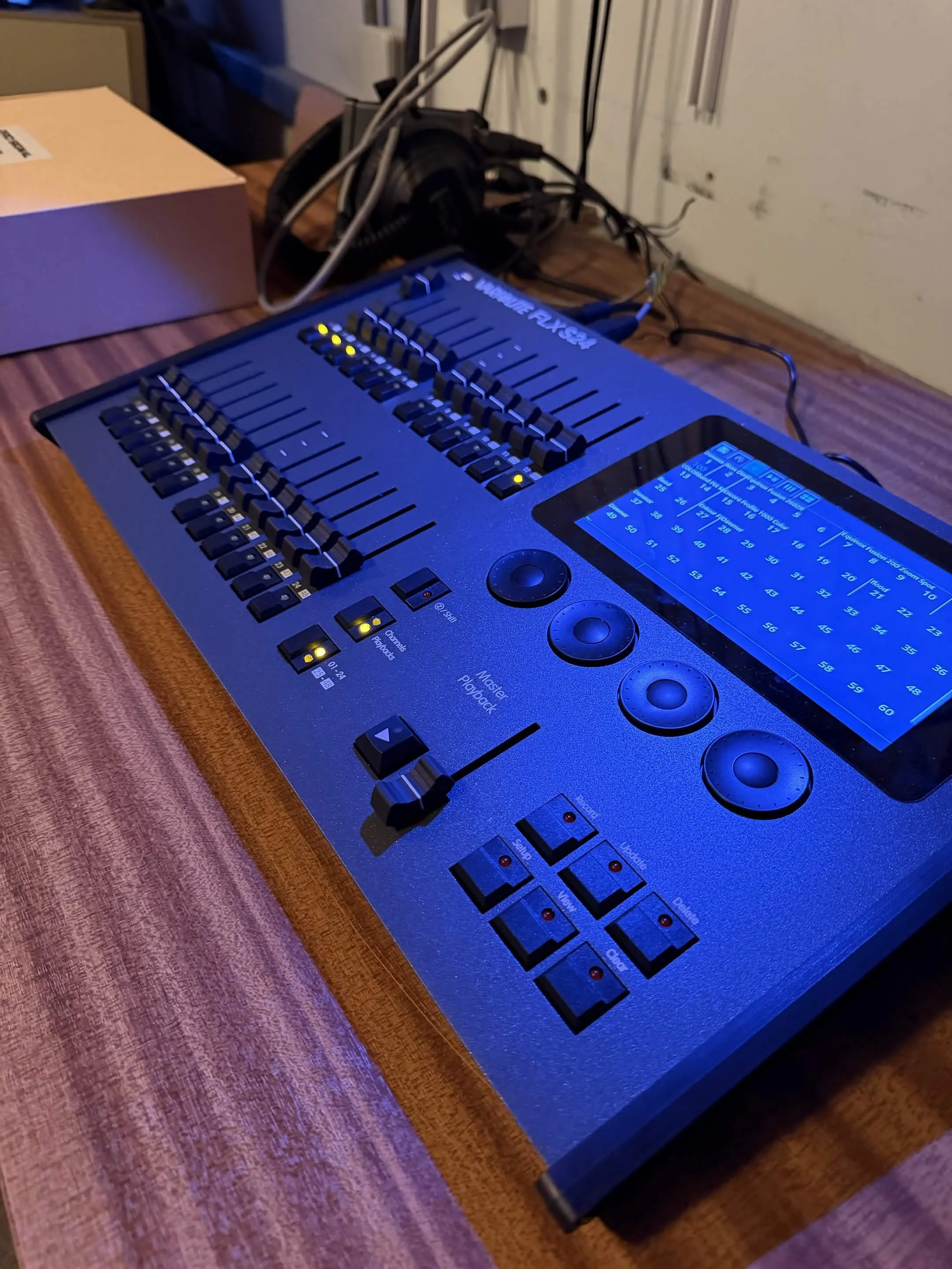 A digital music mixing console with various sliders, knobs, and a touchscreen display on a wooden surface.
