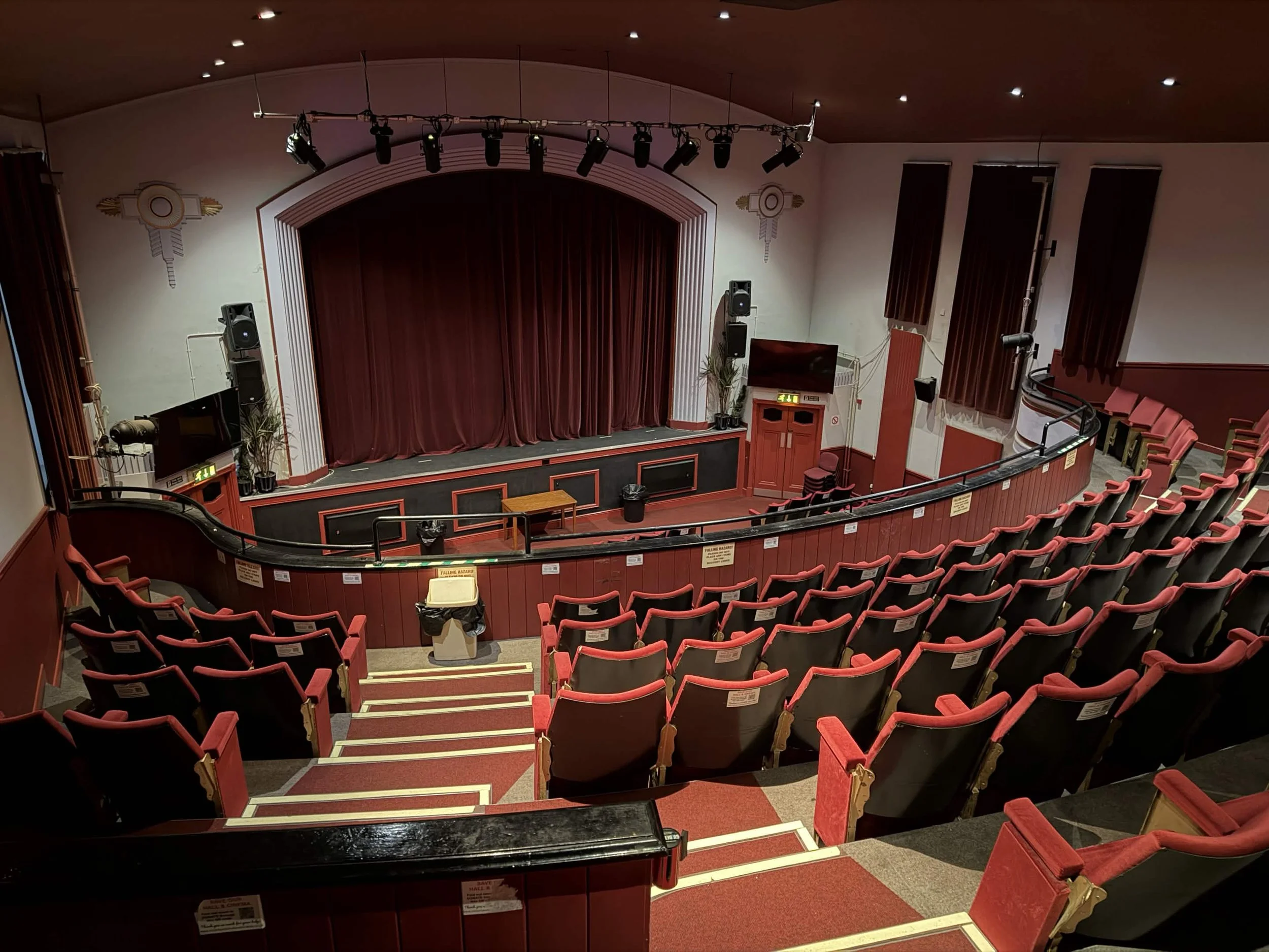 Empty theater with red seats, stage with curtains, and overhead stage lights.