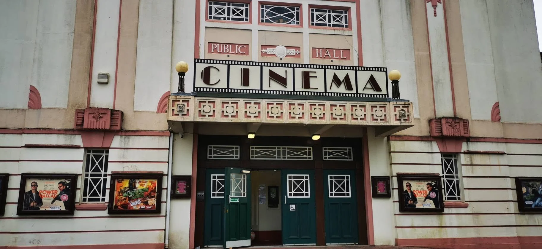Facade of a vintage cinema hall with a sign that reads 'CINEMA'. The building has an art deco style with decorative features and posters for movies displayed near the entrance.