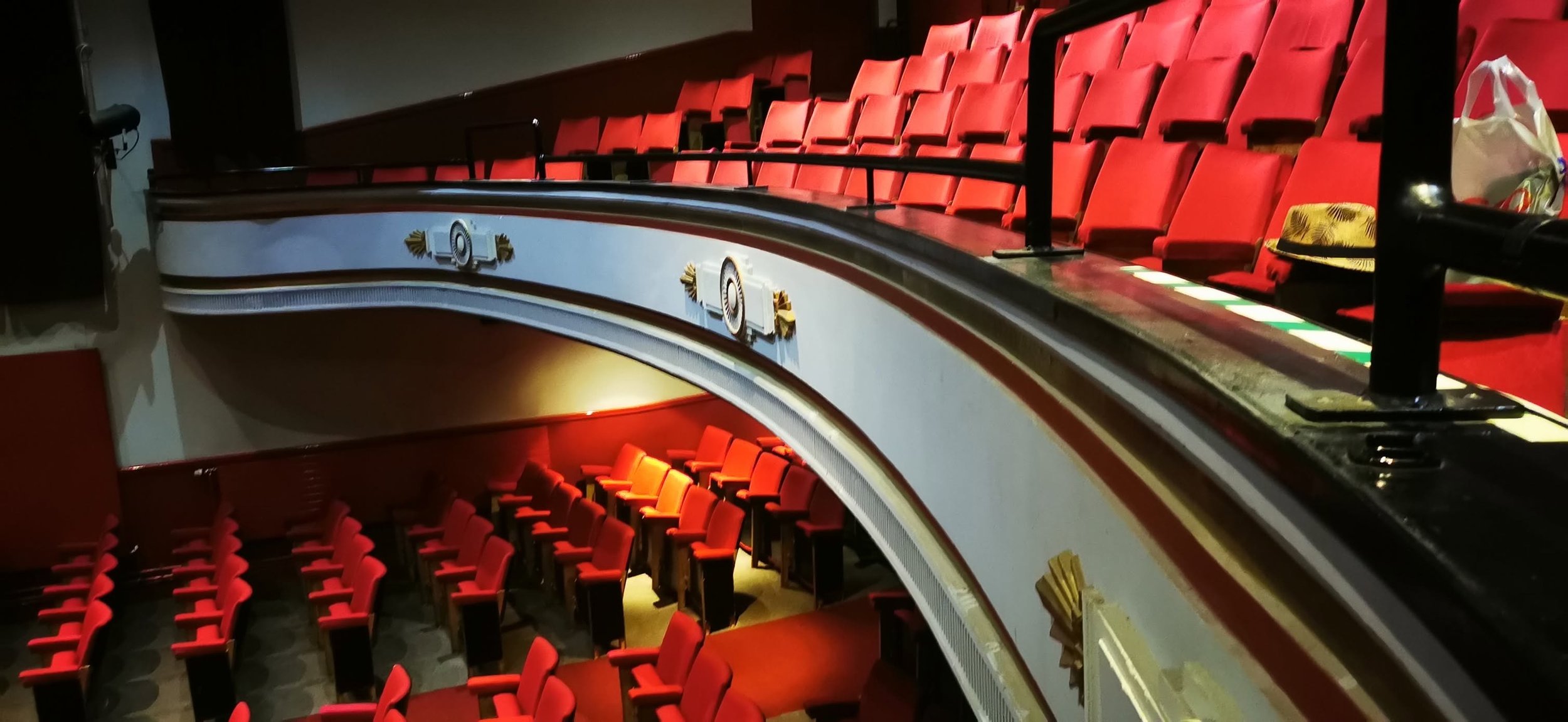 Empty theater with red seats and a decorative balcony railing.
