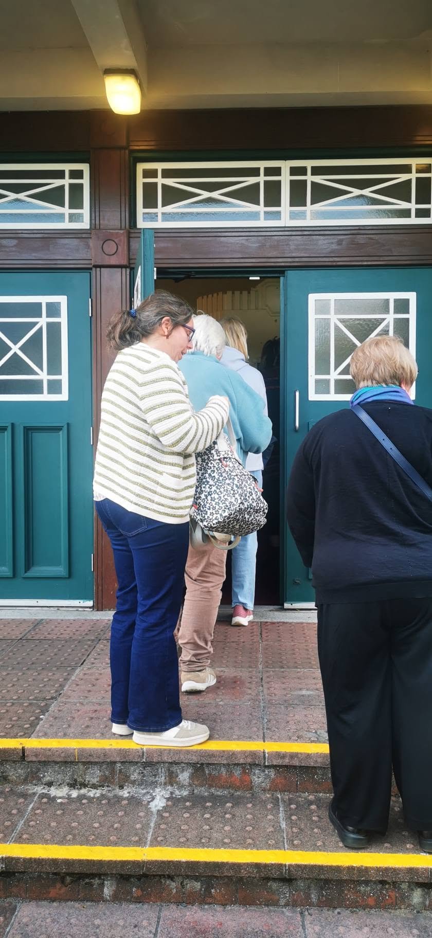 People standing in line outside a doorway, waiting to enter a building. The door is open, revealing the interior.