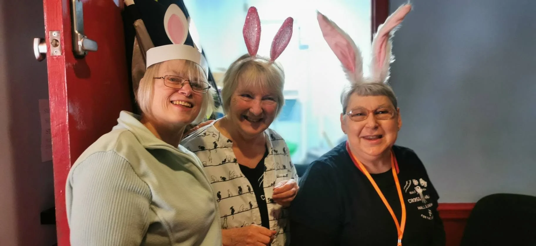 Three women smiling, wearing bunny ears for Easter celebration.