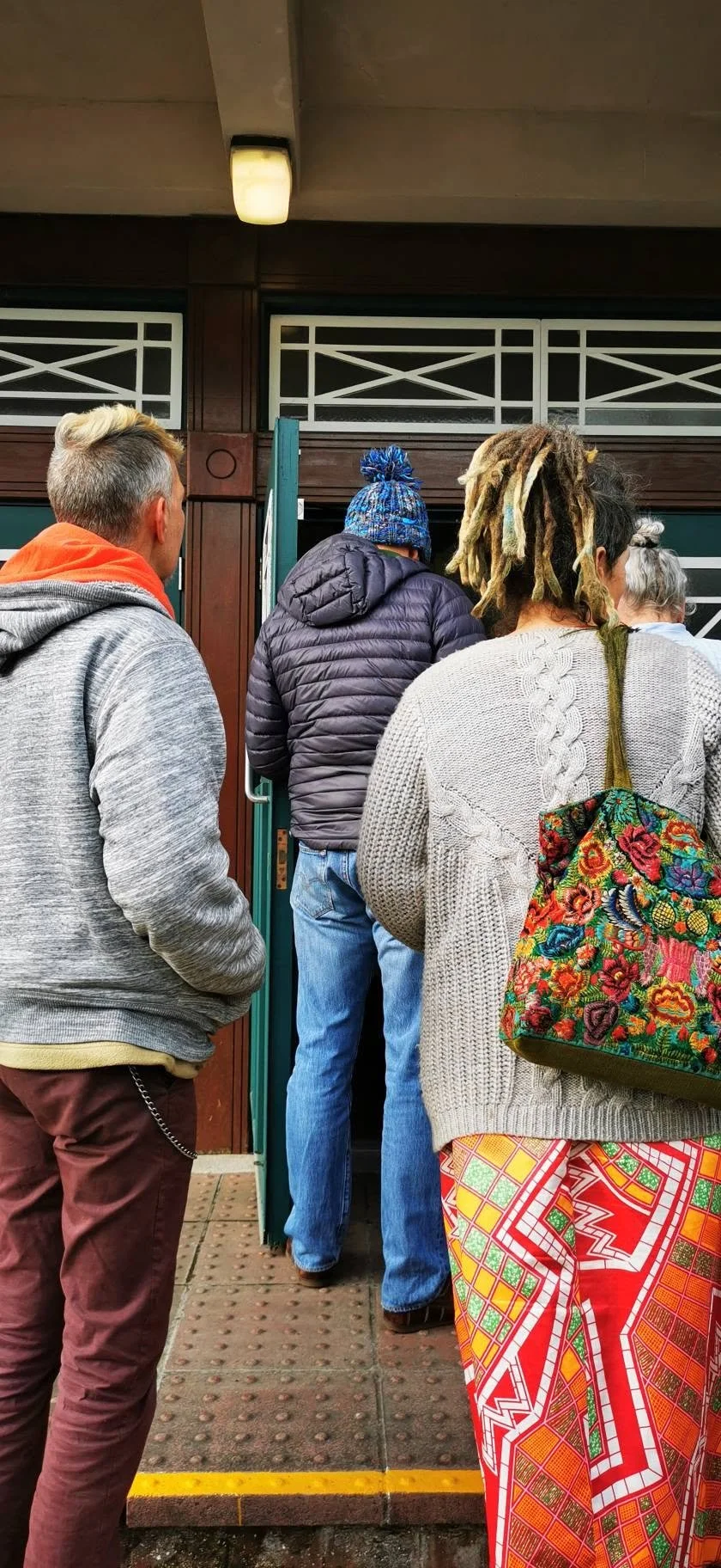 People standing in line outside a building door, waiting to enter.