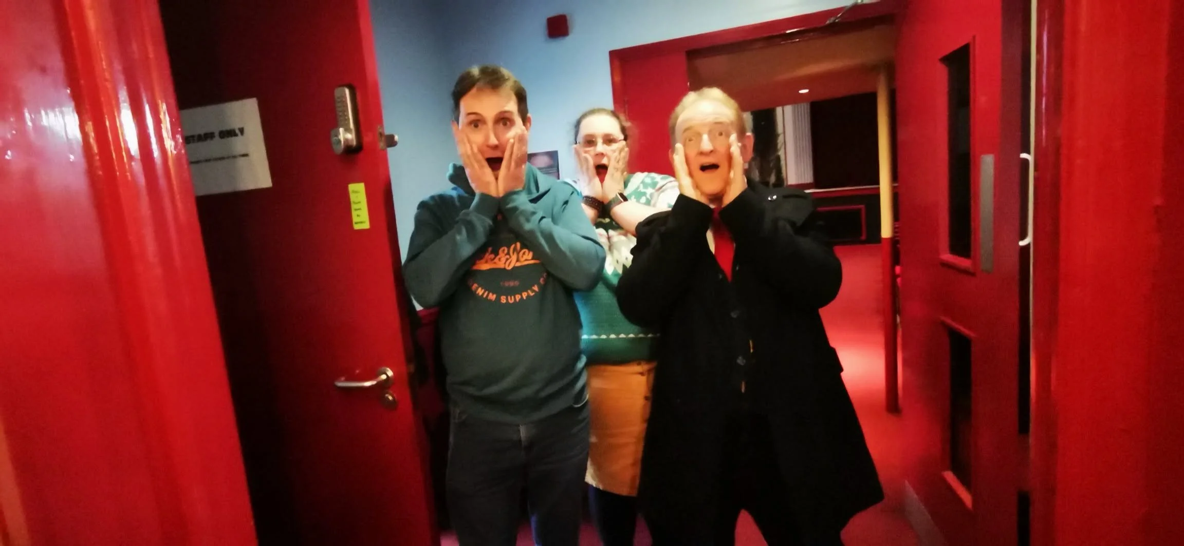 Three people standing inside a red doorframe, holding their faces with surprised expressions.