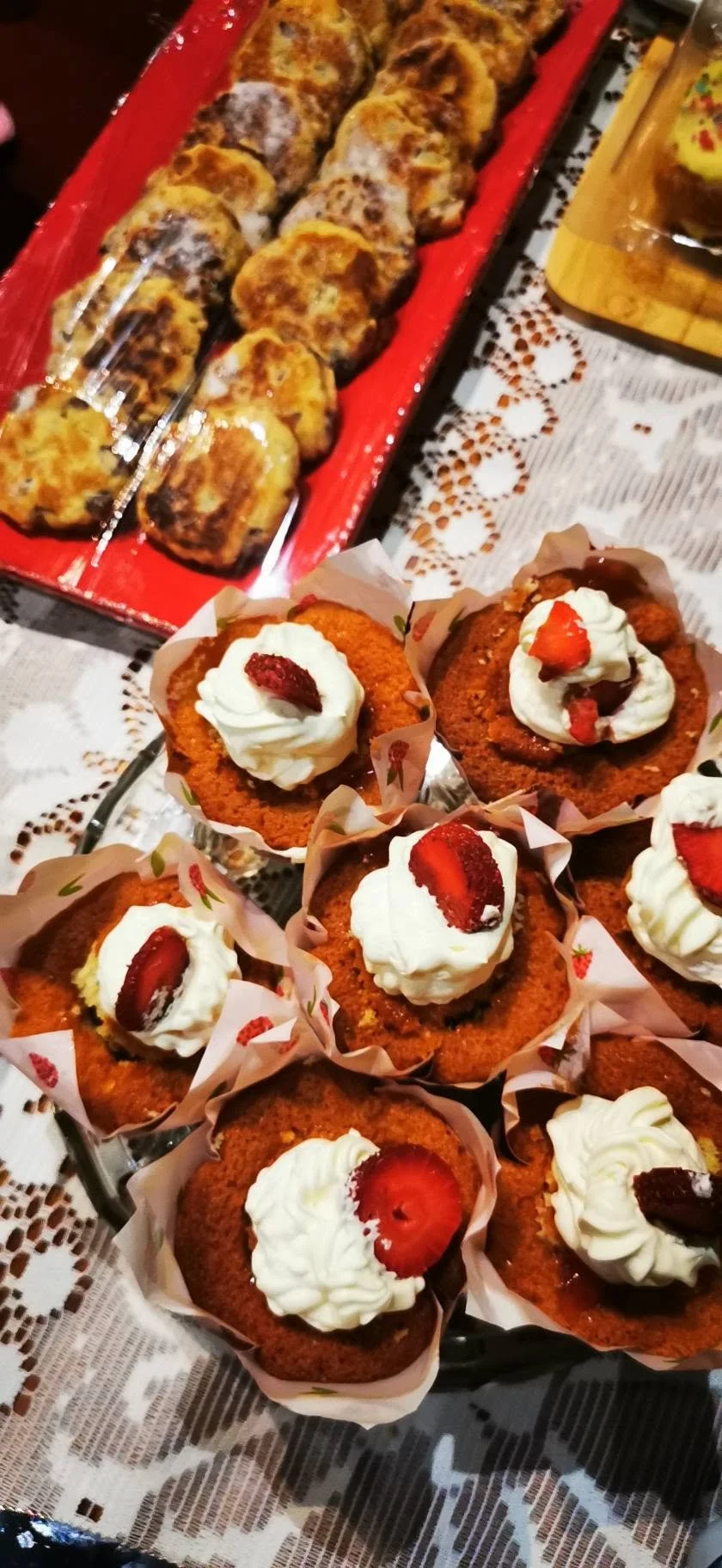 Chocolate cupcakes topped with whipped cream and sliced strawberries, and a tray of baked cheese-stuffed bread rolls or pastries on a red tray.