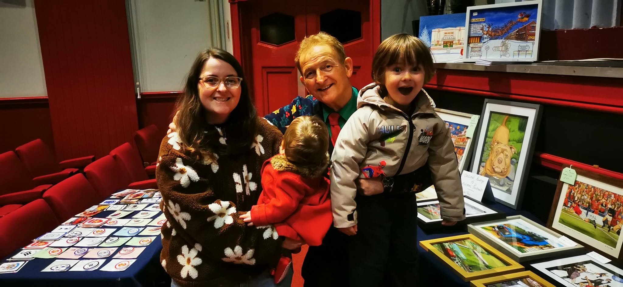 A family of four at an art exhibition, with framed artworks and prints on a table behind them.