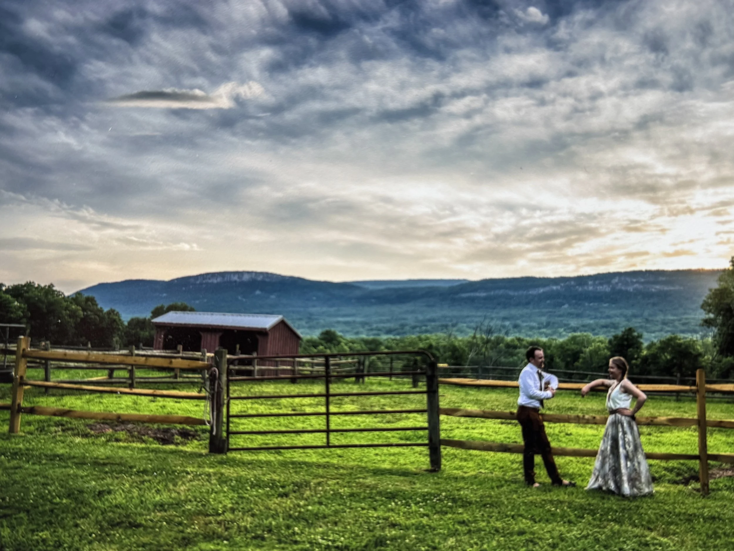 Newlyweds take a beat after saying, "I do." The background features the lush green, farm pastures, the Shawangunk mountains and a dramatic, pre-sunset sky.