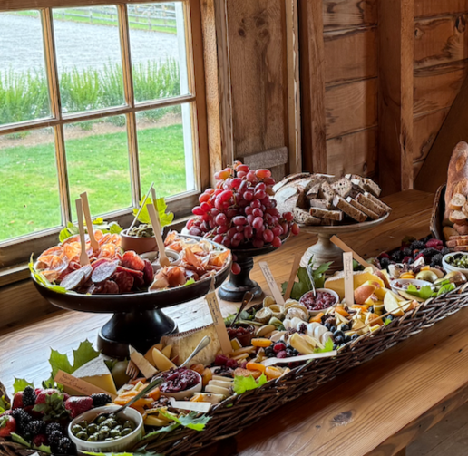 Charcuterie platter with strawberries, grapes, cheese, crackers, and olives near a window with farm views at La Luna's upstairs event space.