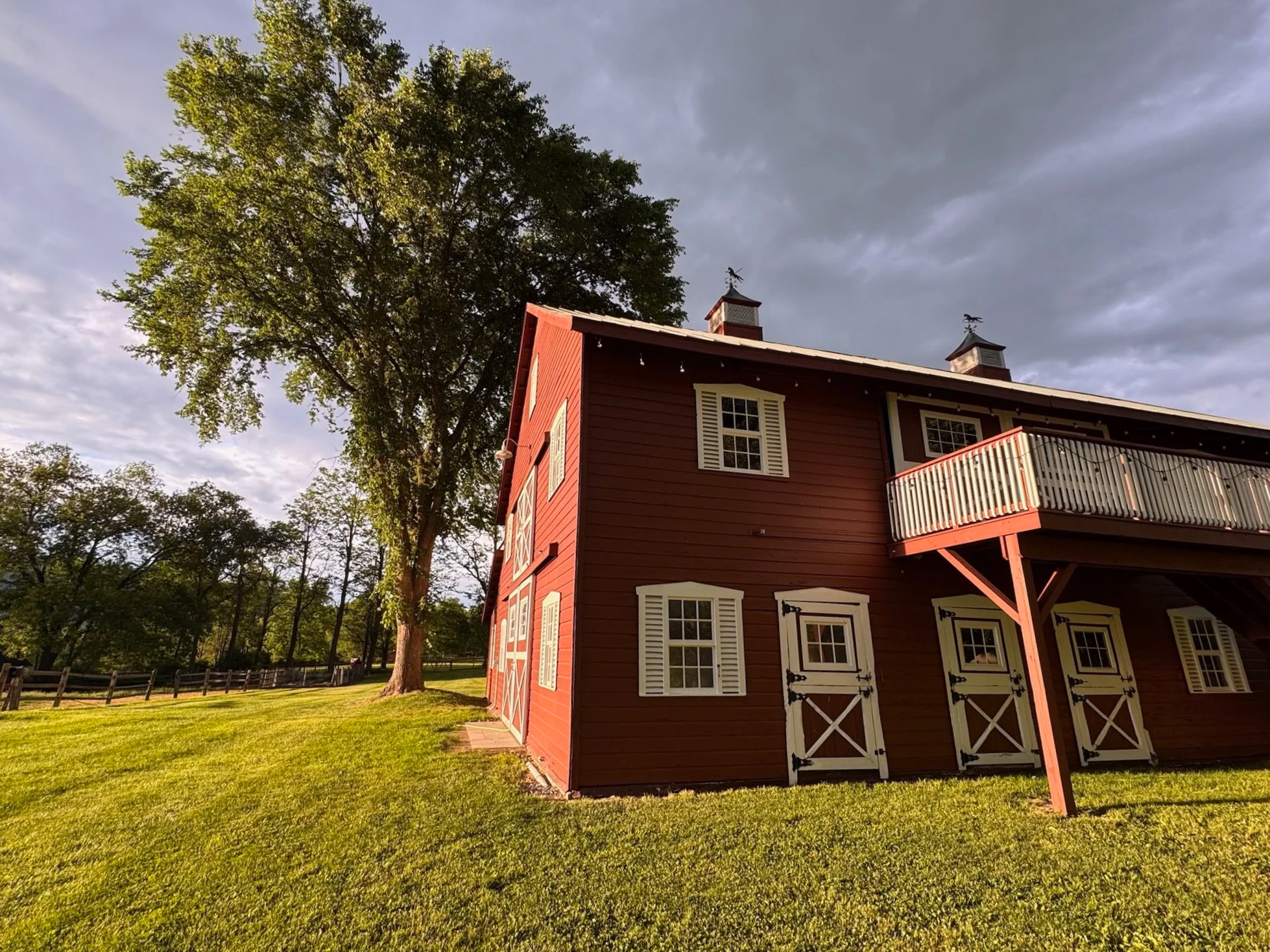 Amish-built, event barn with white shutters and black decorative hinges under a Hudson Valley sky, surrounded by green grass and trees at La Luna Farm.