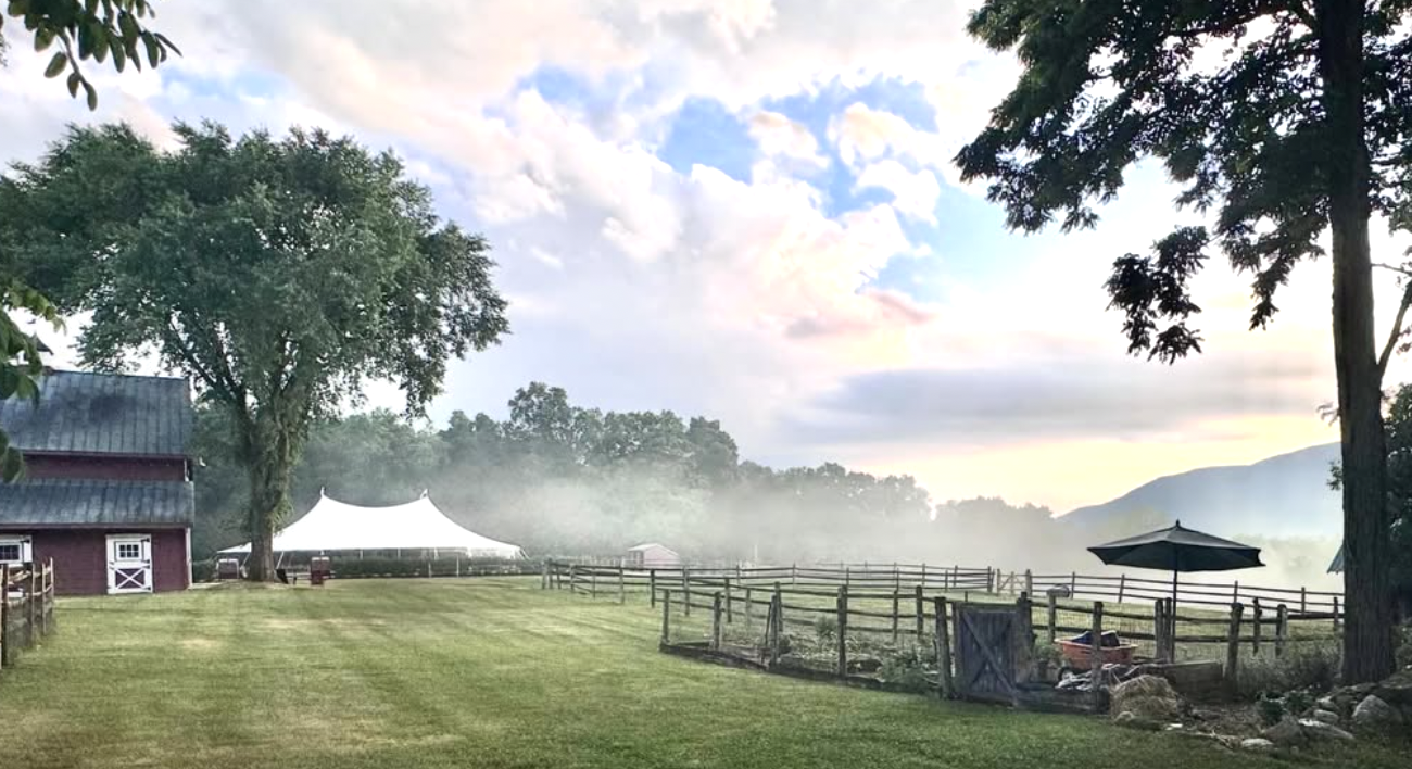 Foggy morning and blue sky, a barn, and white sailcloth tent await a wedding celebration.