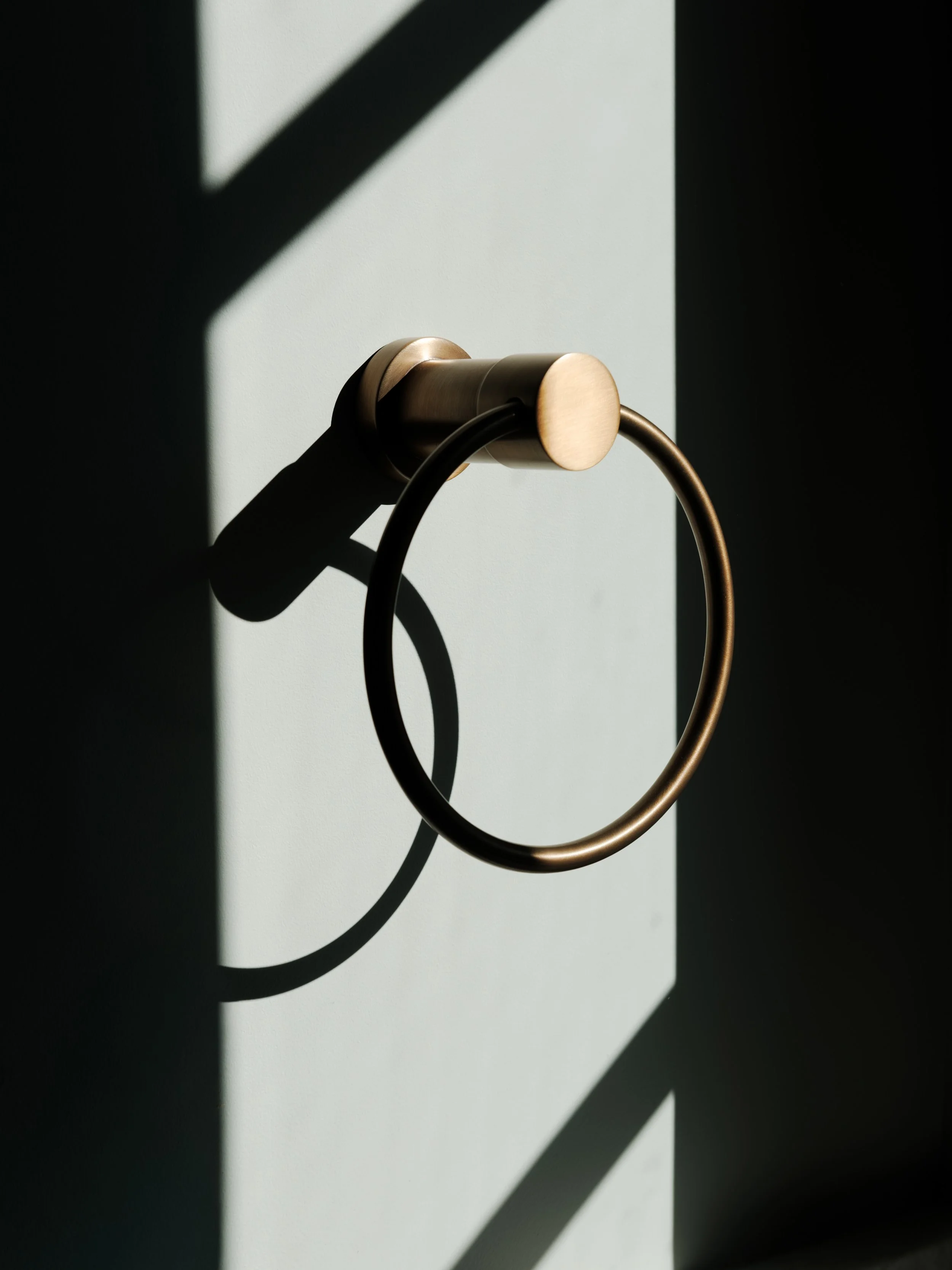 Close-up of a metallic towel ring mounted on a wall with shadow play and light contrast.