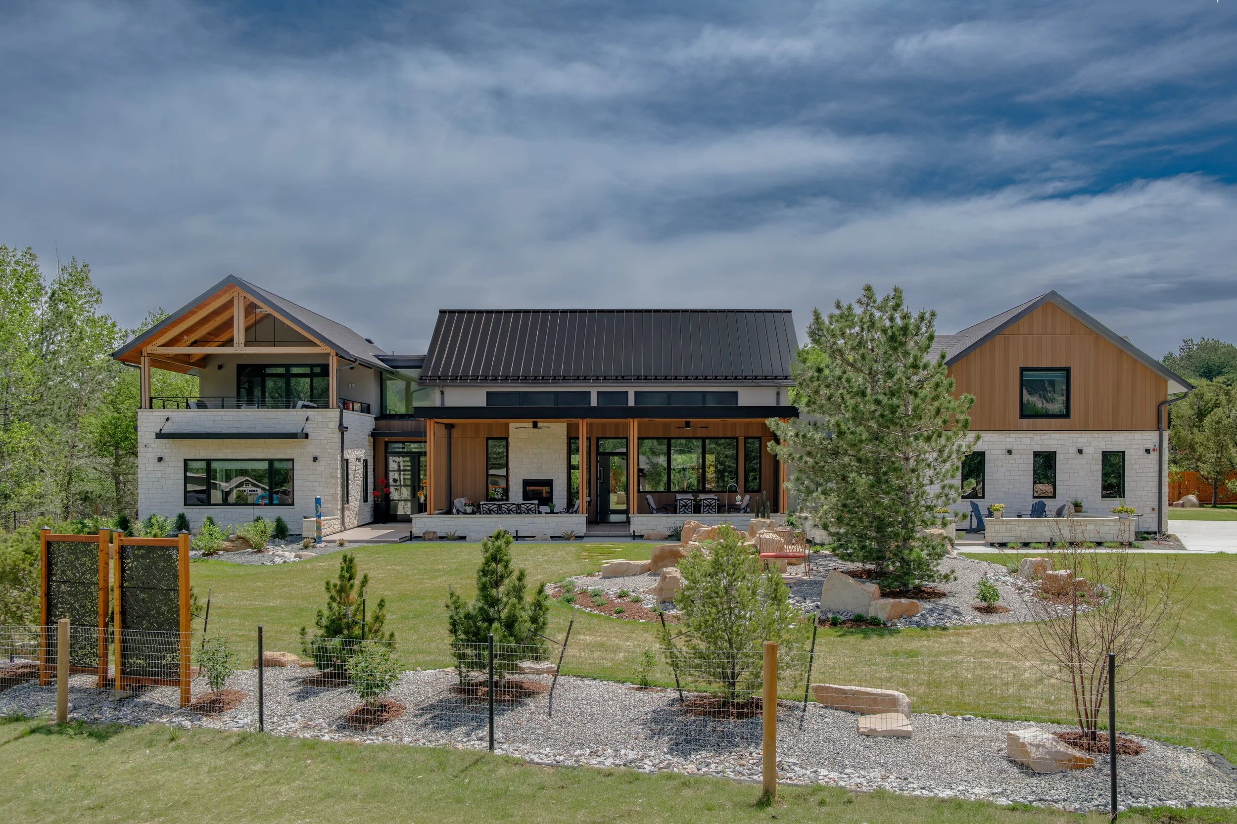 Modern house with a large backyard, trees, and a landscaped garden under a partly cloudy sky.