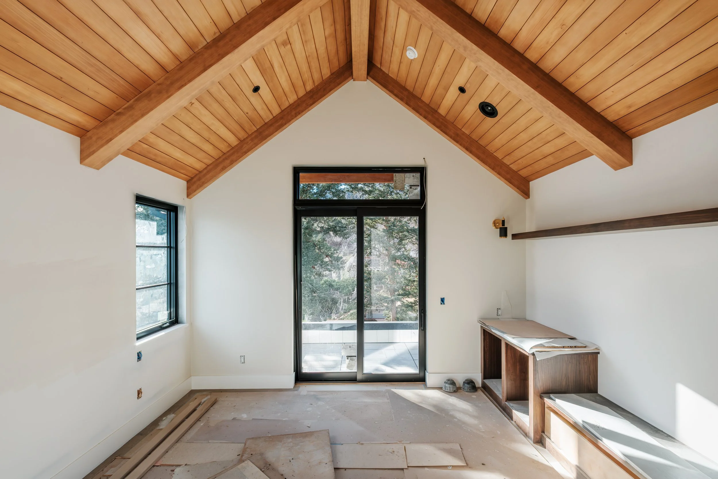 Interior room under construction with a wood-paneled vaulted ceiling, large window, sliding glass door, and unfinished floor and cabinetry.