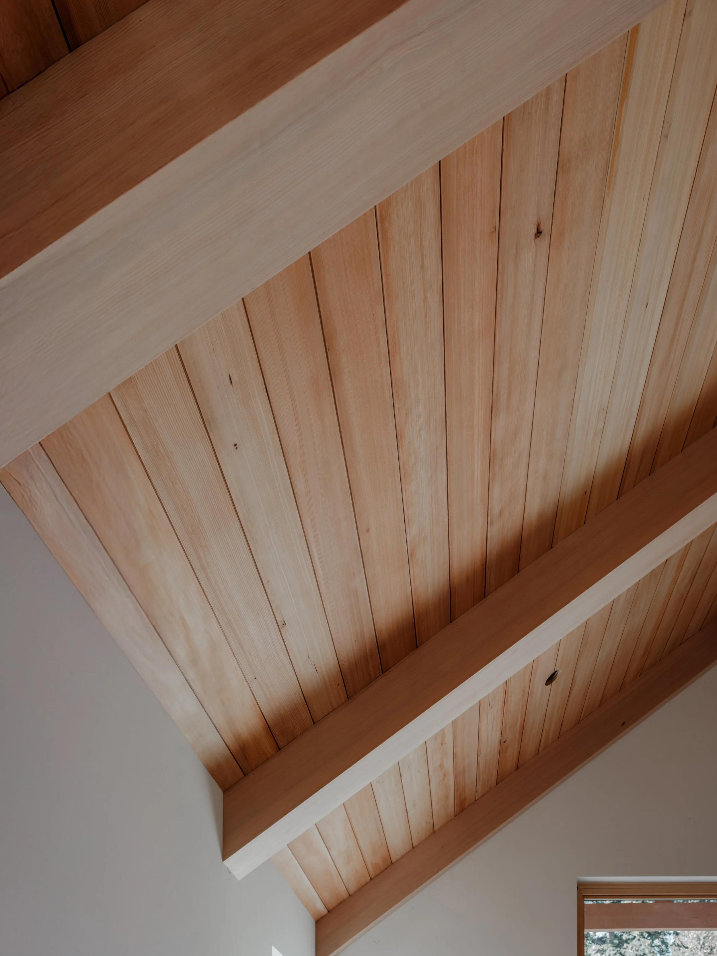 Wooden ceiling with exposed beams and a small window showing trees outside.