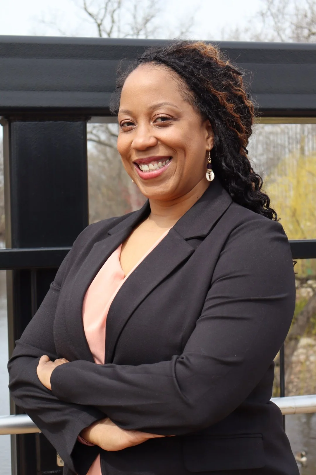 Smiling woman with curly hair in professional attire outside with trees in the background.