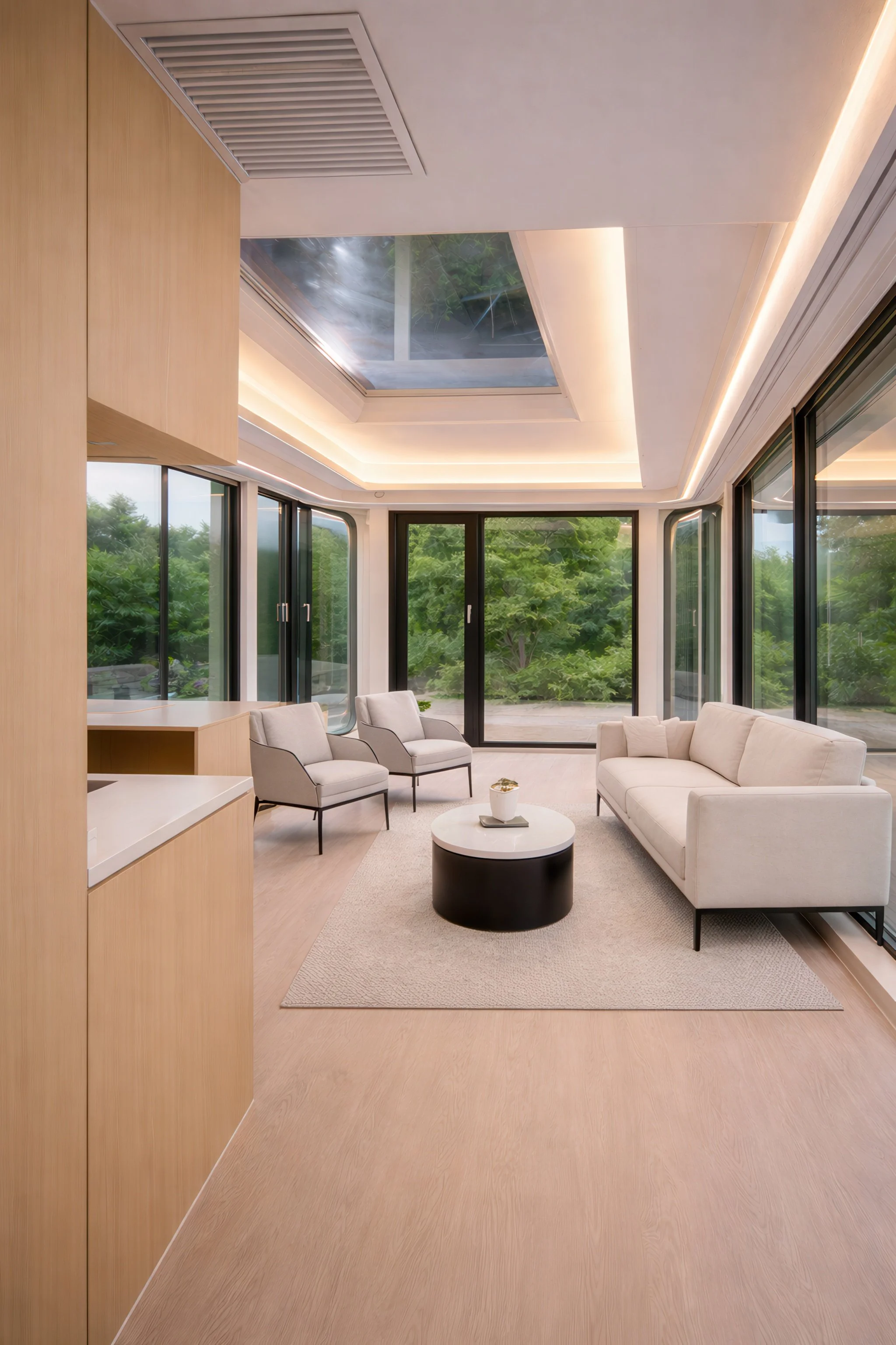 Modern living room with large windows, a skylight, white sofa, two armchairs, a round coffee table, and a light wood floor.