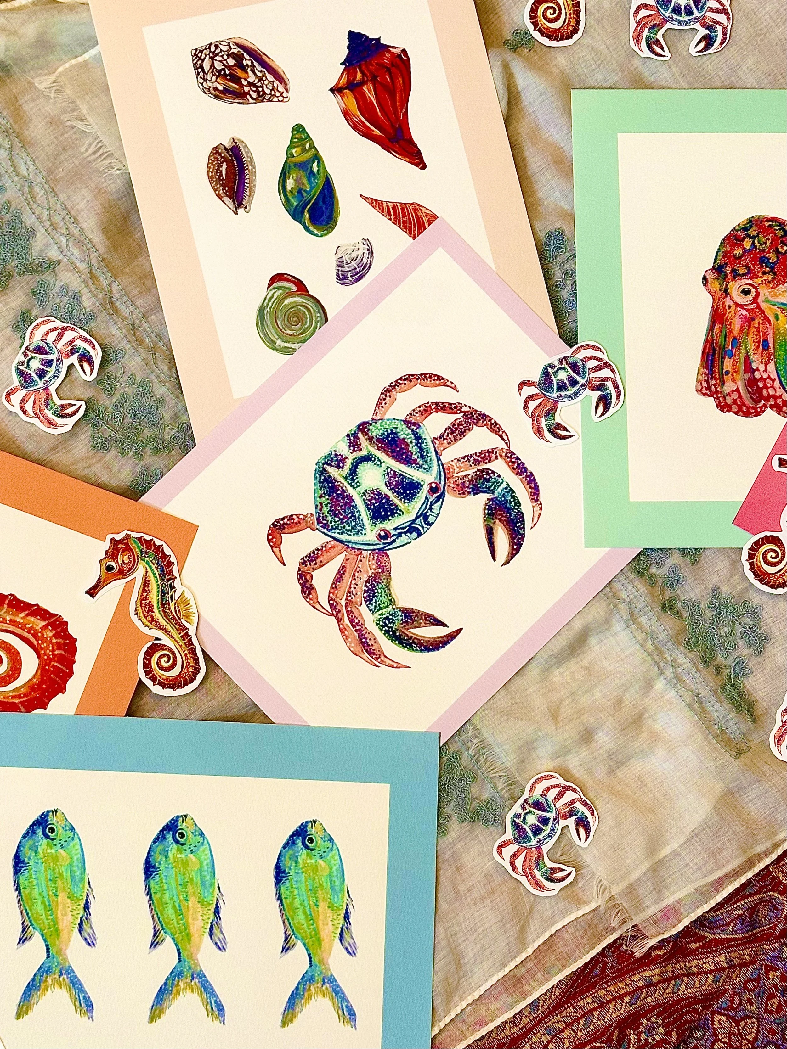 Colorful drawings of sea creatures, including crabs, seashells, fish, and turtles, displayed on colorful construction paper and stickers on a table with a patterned cloth.