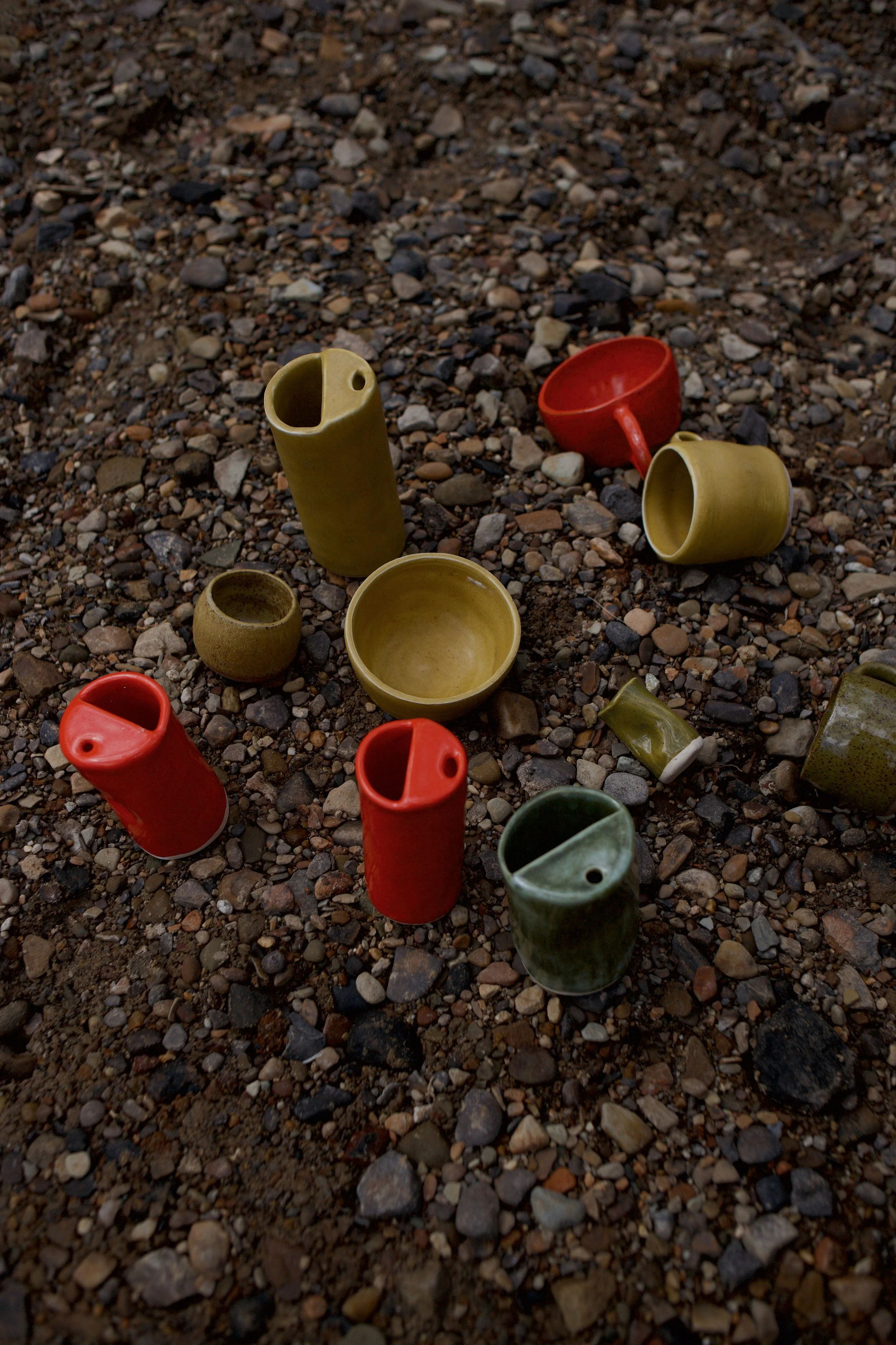 Various colorful ceramic cups and mugs scattered on a gravel ground.