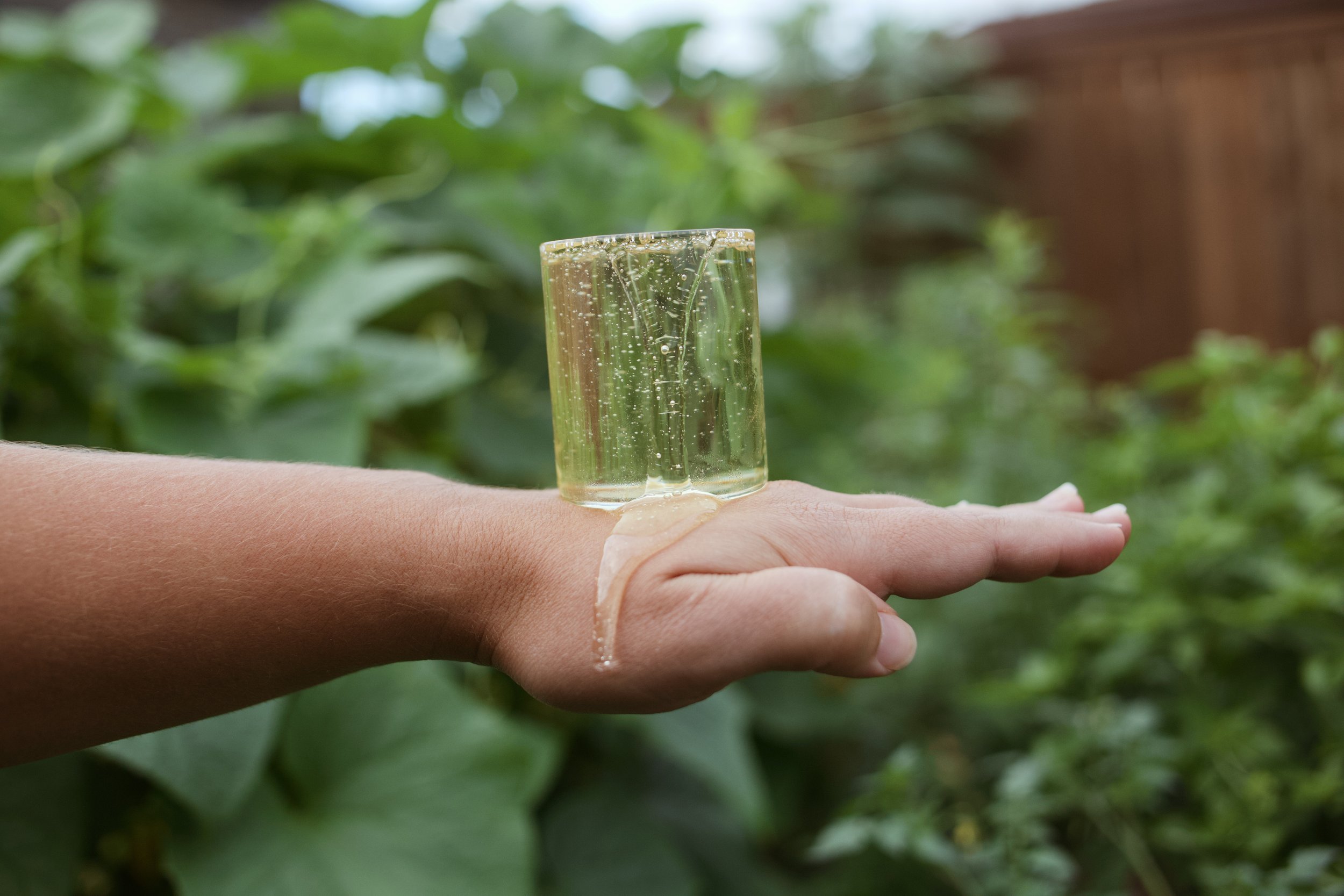 A person's hand holding a small glass filled with sparkling water outdoors.