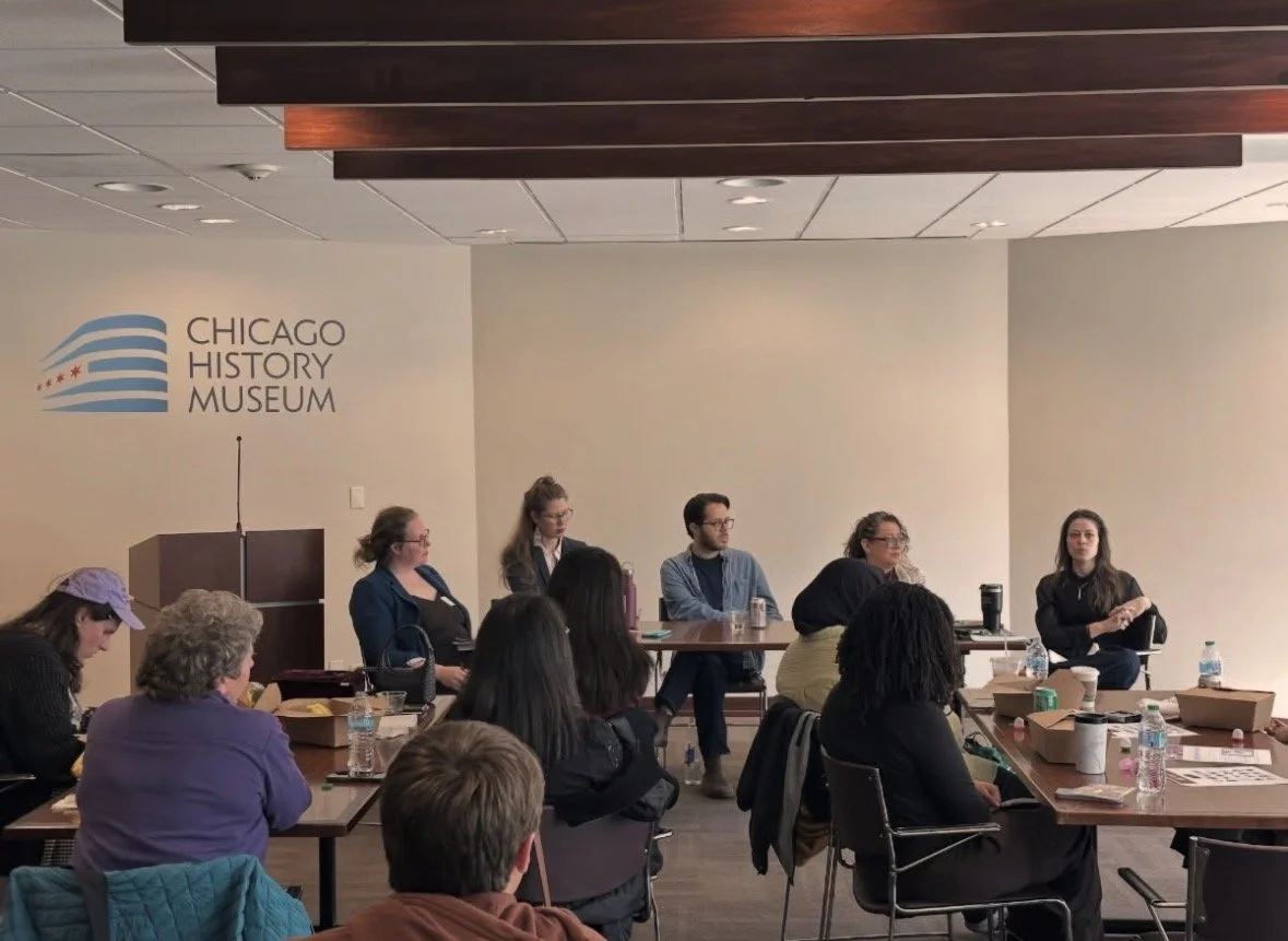 A group of people attending a panel discussion at the Chicago History Museum, with five panelists sitting at the front and audience members seated at tables.