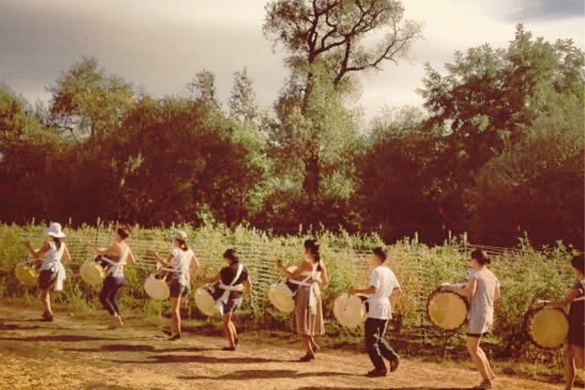 A group of people playing drums in an outdoor setting with trees in the background.