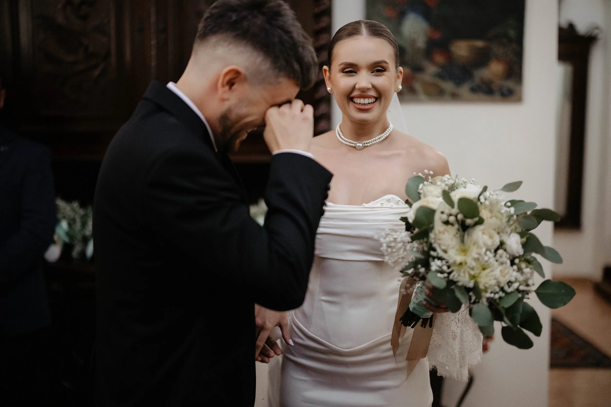 A bride and groom at their wedding ceremony, with the bride smiling and holding a bouquet of flowers.