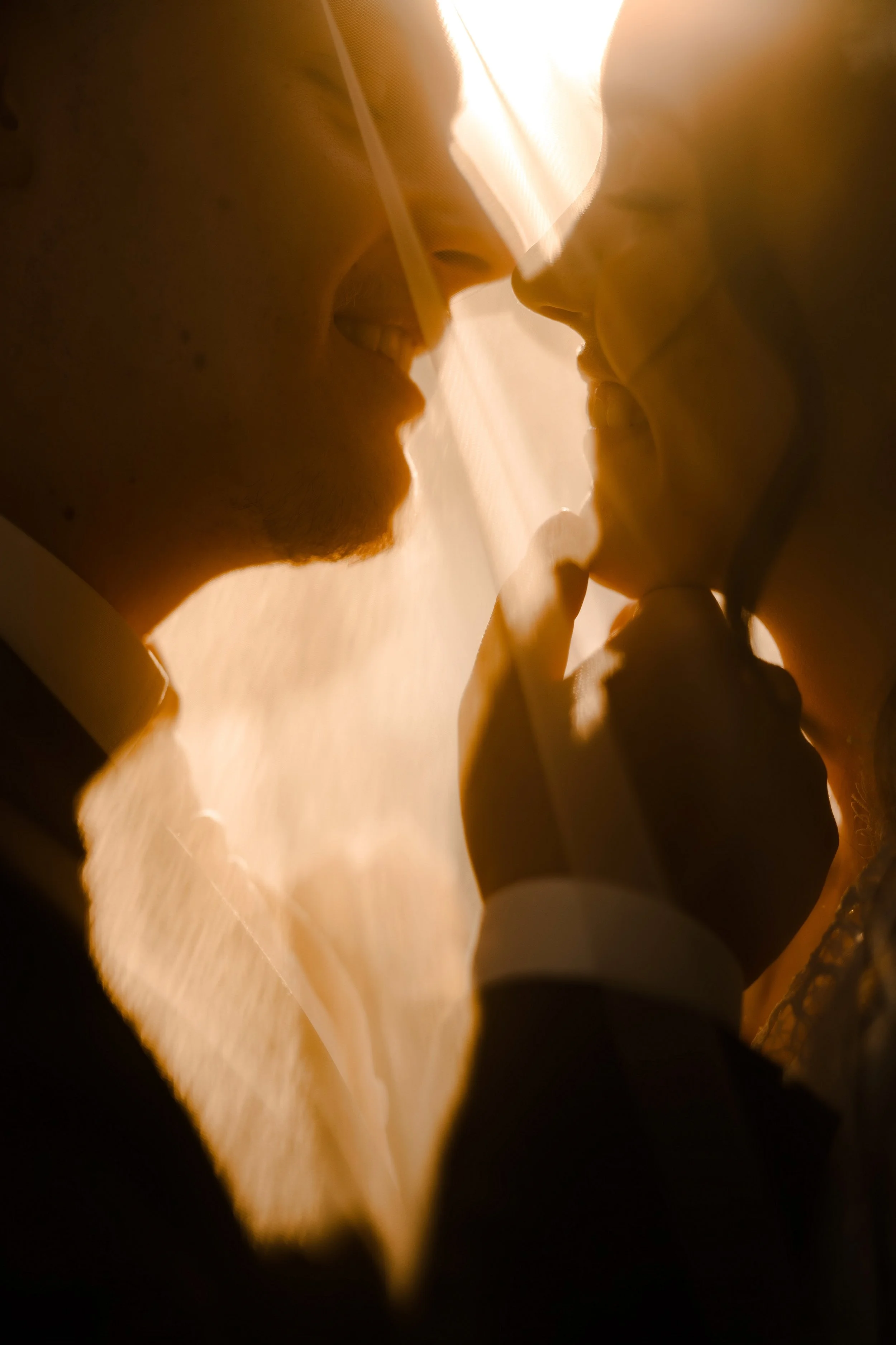 Close-up of a man whispering into a woman's ear, both smiling, with warm lighting.