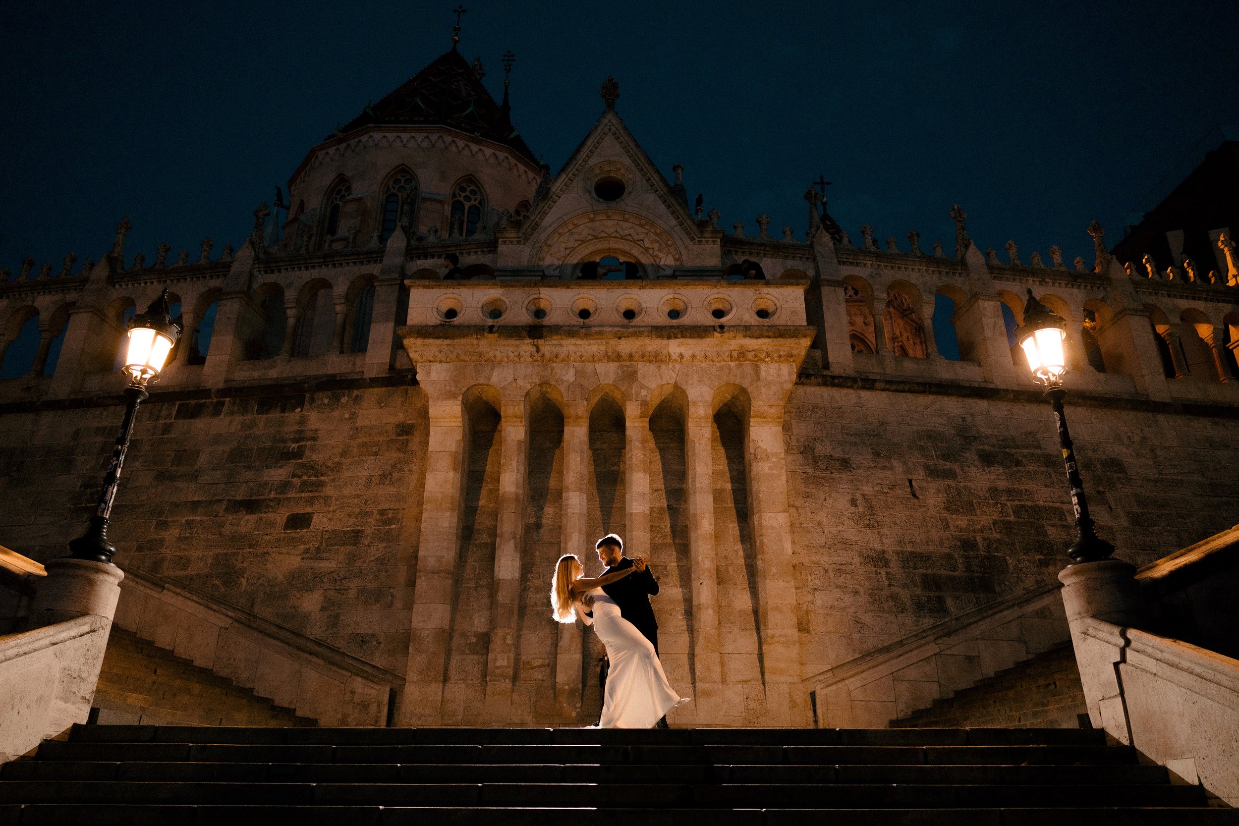 A couple dancing on the steps in front of a historic building at night, illuminated by streetlights.