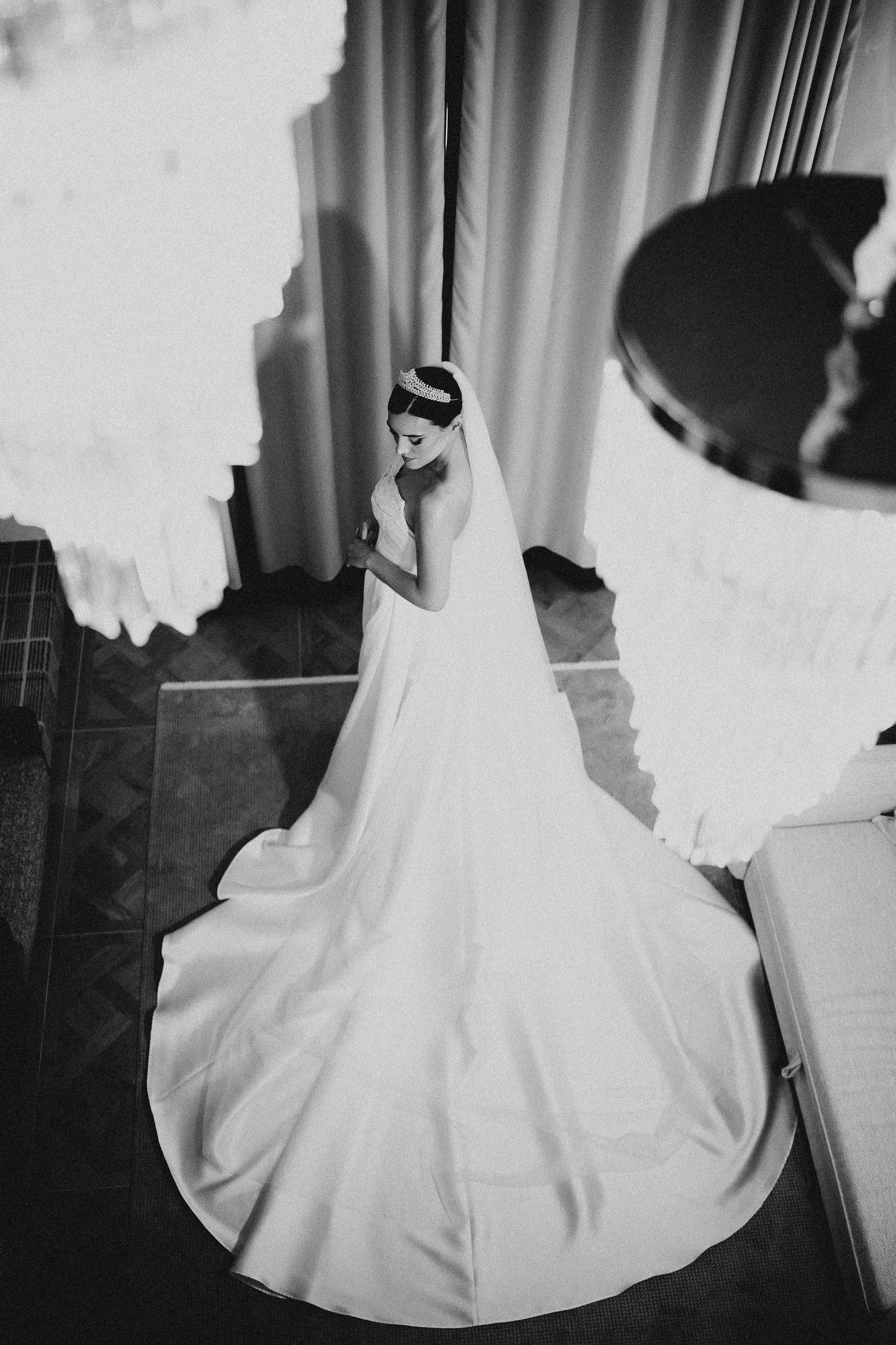 A bride in a wedding dress and tiara standing under a veil as seen from above.