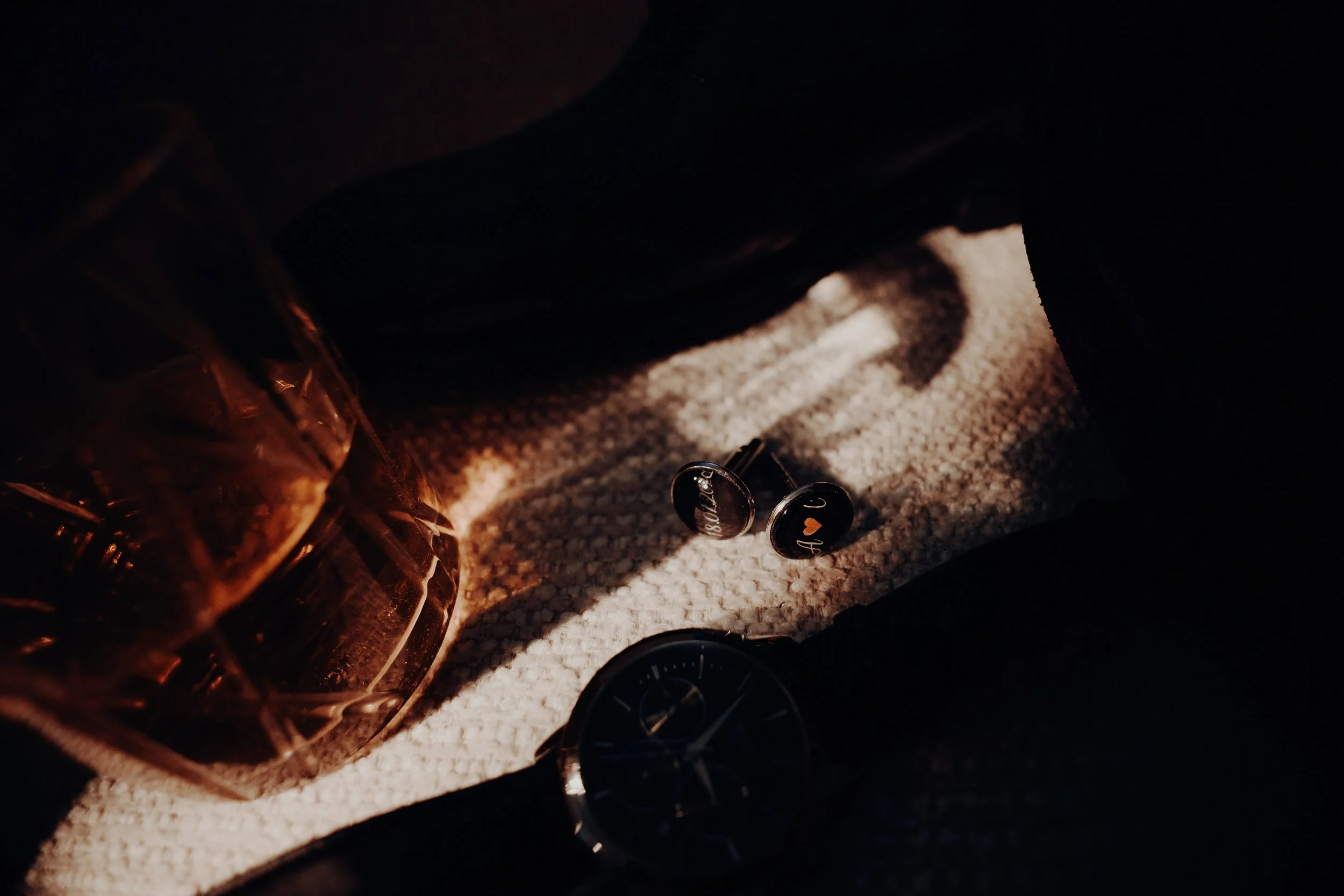 Close-up of a wine bottle, two black caps with a Mona Lisa illustration, a wristwatch, and a pair of black shoes on a beige carpet.