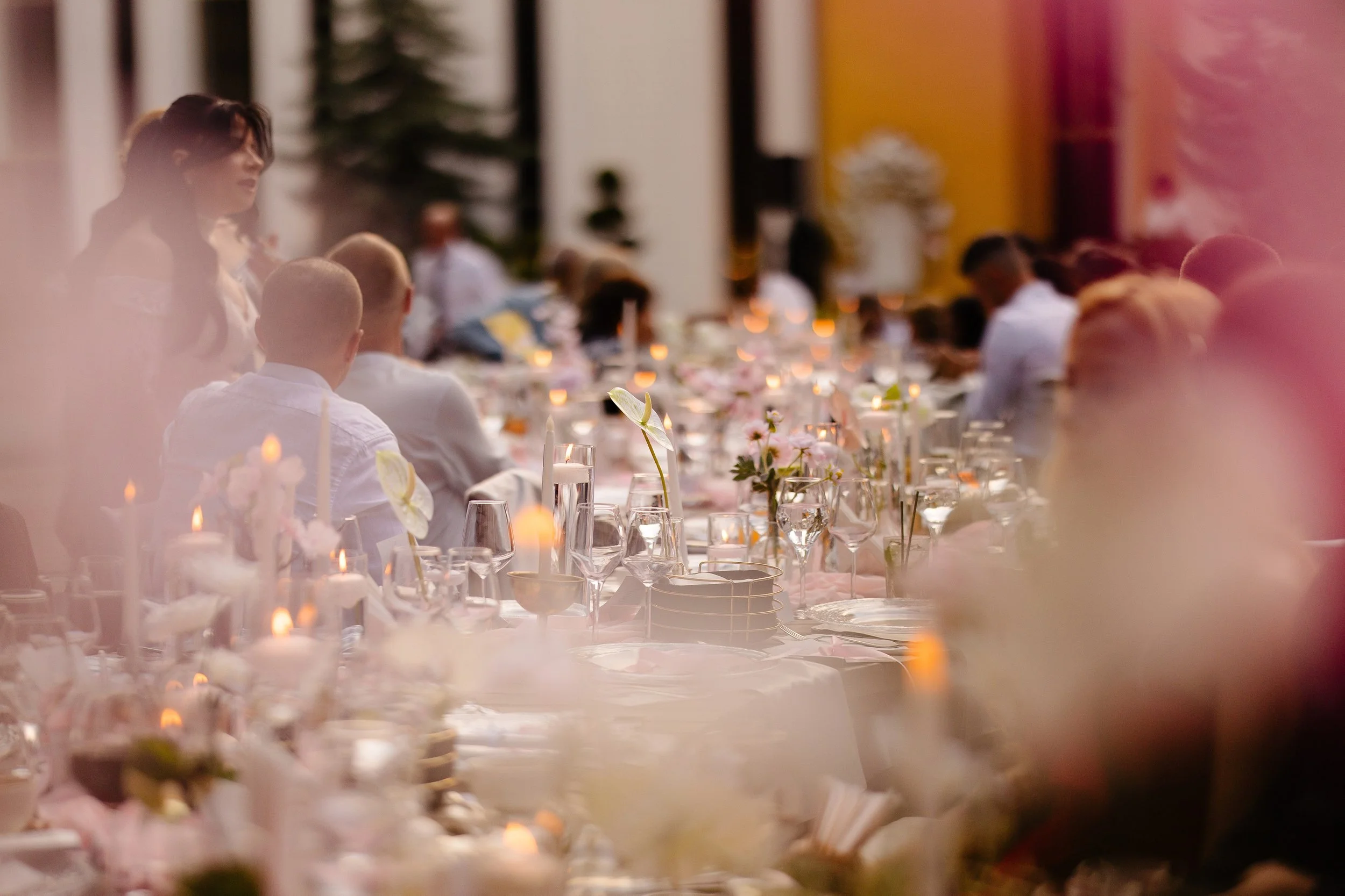 A woman at a banquet table with many glasses, candles, and flowers, indoor, evening, blurred background.