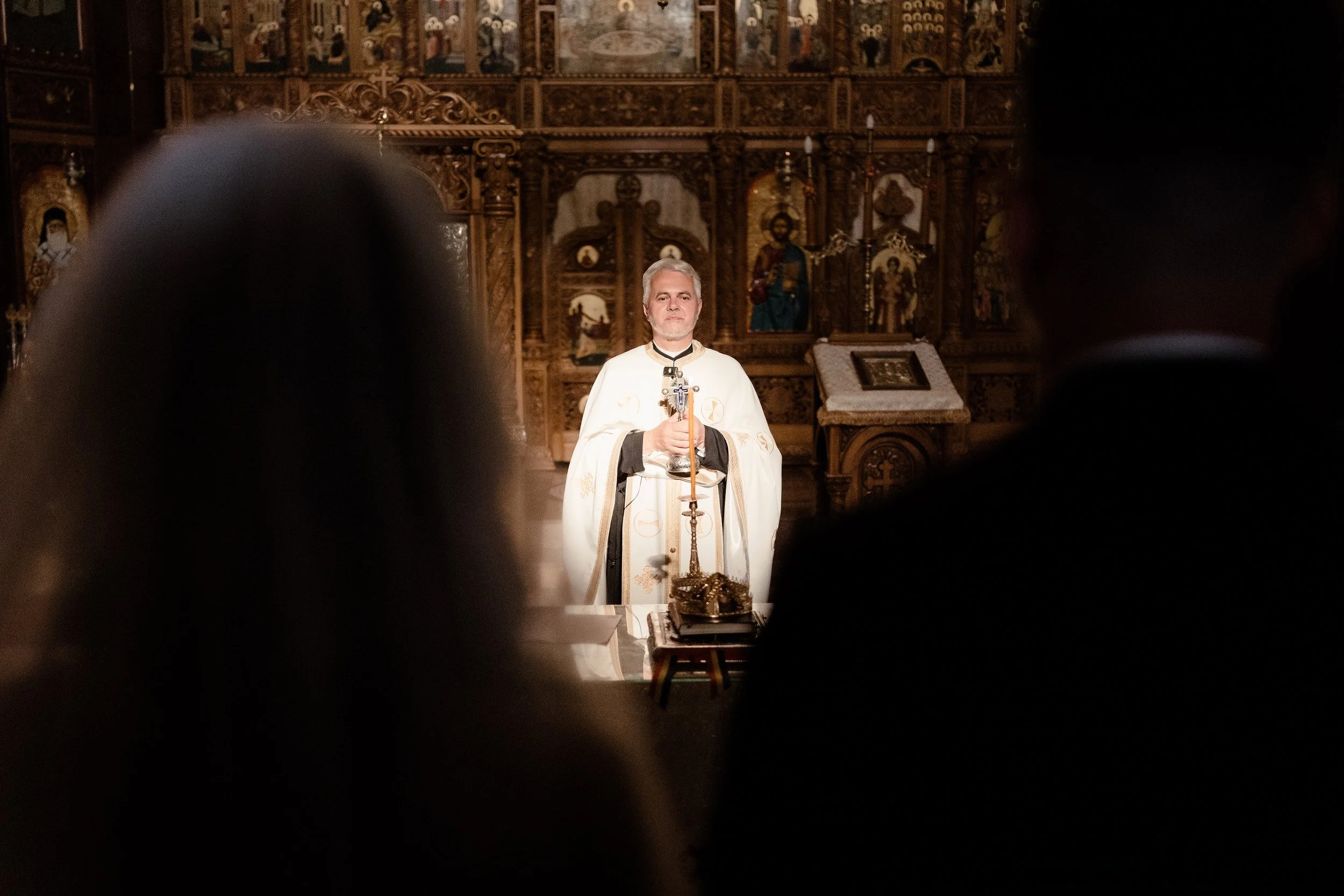 A man dressed in religious robes standing in a church with an ornate wooden altar in the background.