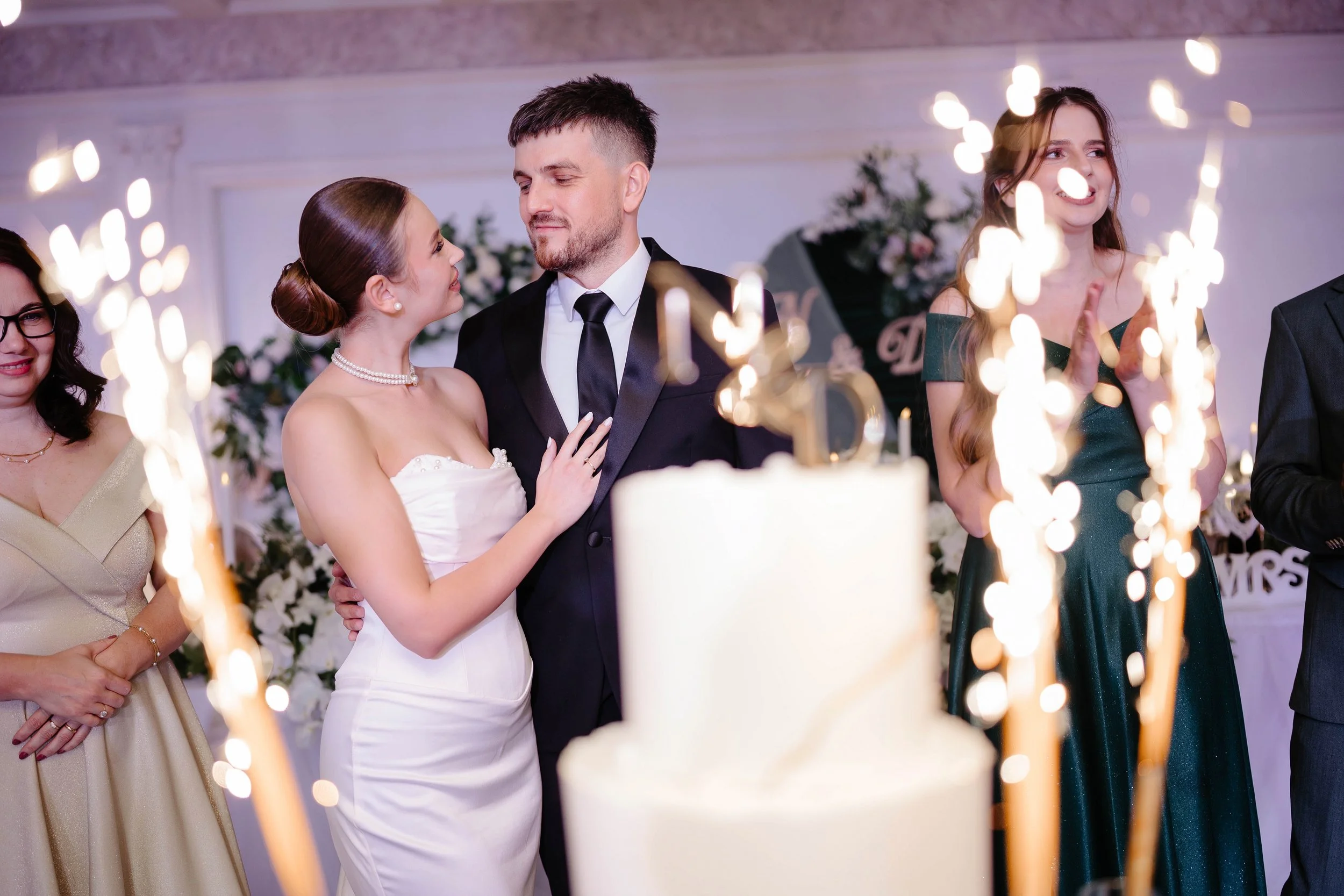 A bride and groom dancing at their wedding reception, surrounded by friends and family, with sparklers in the foreground.