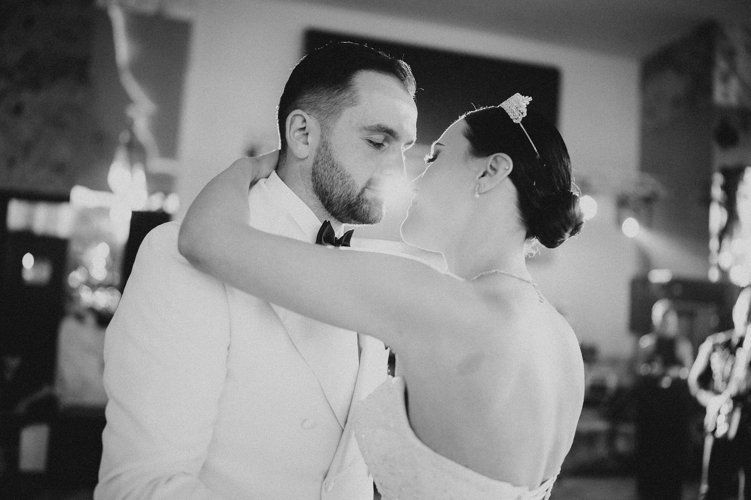 A black and white photo of a bride and groom embracing and about to kiss at their wedding reception.
