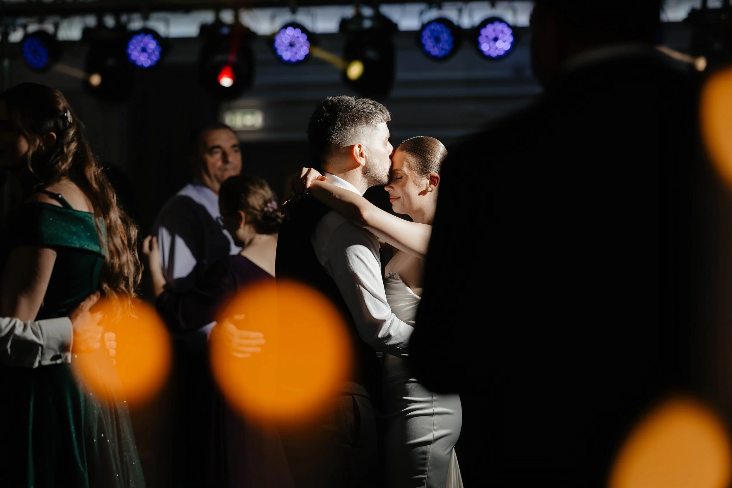 A couple sharing a romantic moment while dancing at a formal event with colorful stage lights overhead