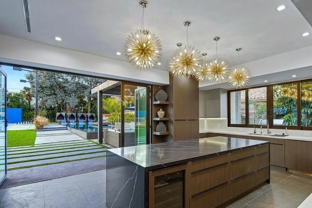 Contemporary kitchen featuring wood cabinets, dark stone island, built-in appliances, and starburst pendant lighting