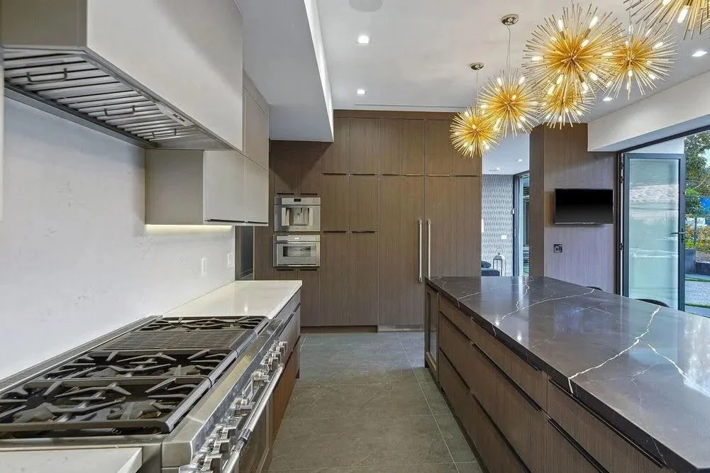 Contemporary kitchen featuring wood cabinets, dark stone island, built-in appliances, and starburst pendant lighting