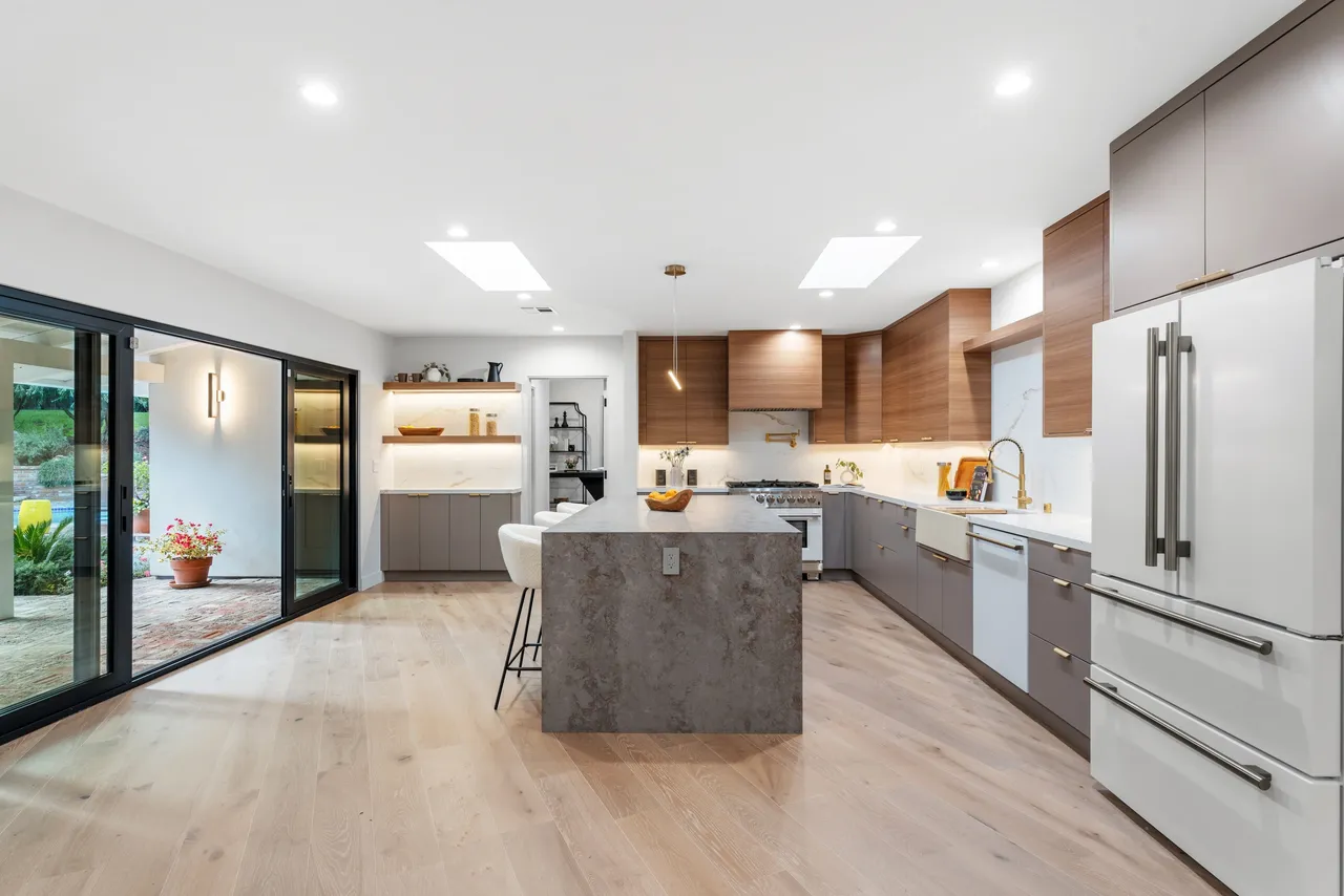 Wide view of modern Los Angeles kitchen showcasing wood‑grain cabinetry, gray uppers, and open layout