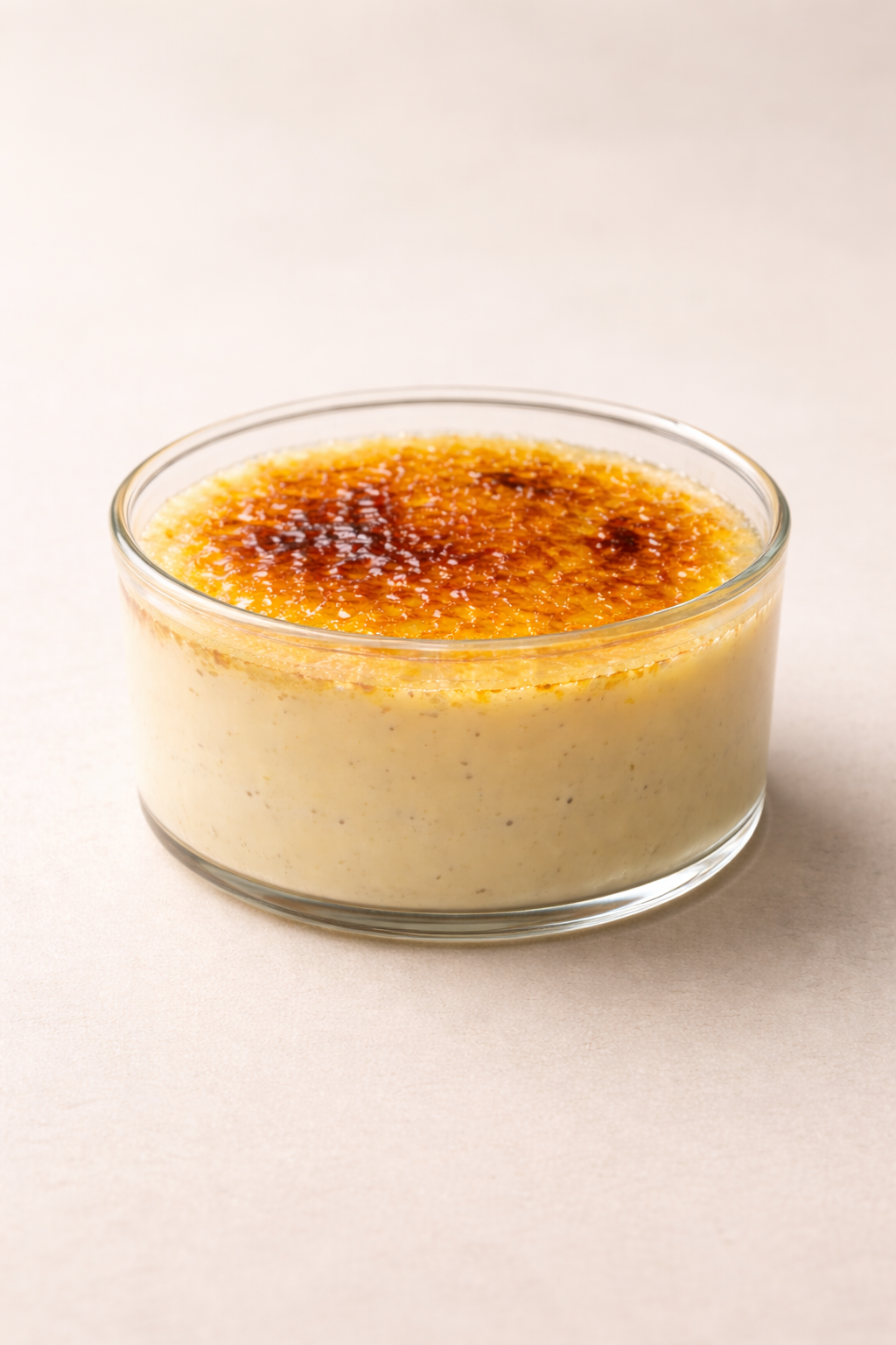 A glass bowl of crème brûlée with a caramelized sugar crust on top, placed on a light background.