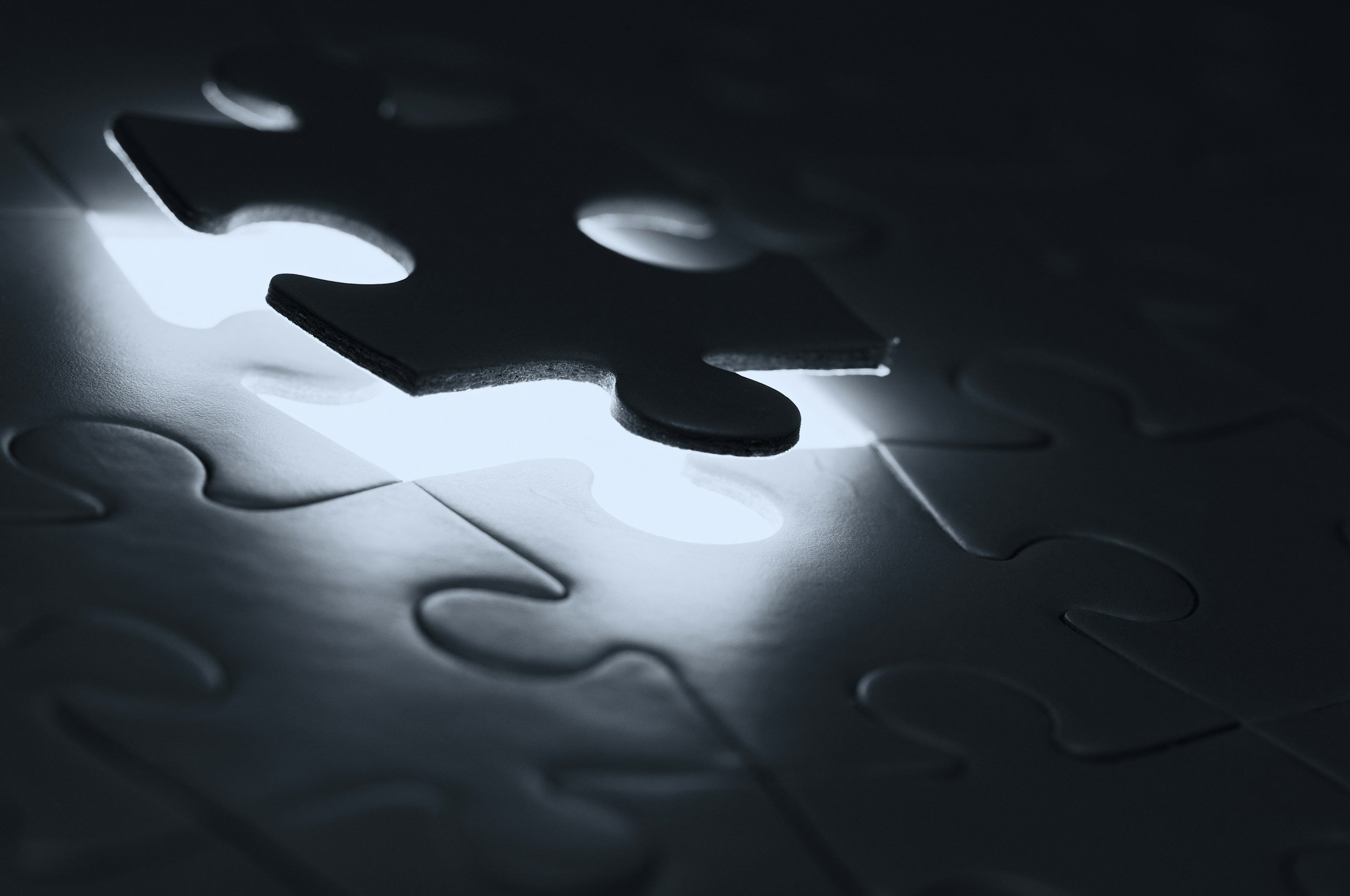Close-up of interconnected puzzle pieces with a glossy, reflective surface, showing a gap between the pieces, illuminated by light from below.