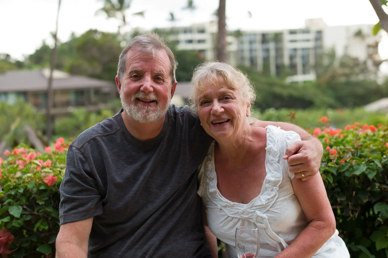 Happy man with arm around woman, with tropical bushes in background.
