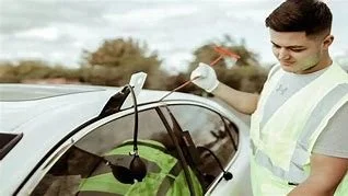 A man wearing a safety vest opening the car door of a white vehicle.