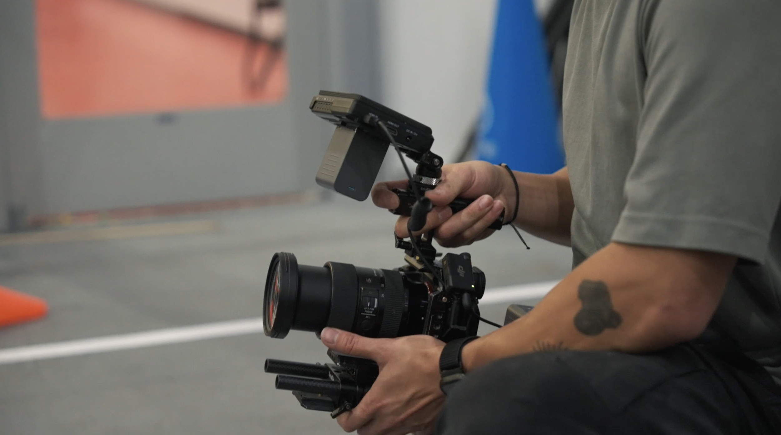 Close-up of a person holding a professional camera with a mounted monitor and stabilizer, in an indoor setting.