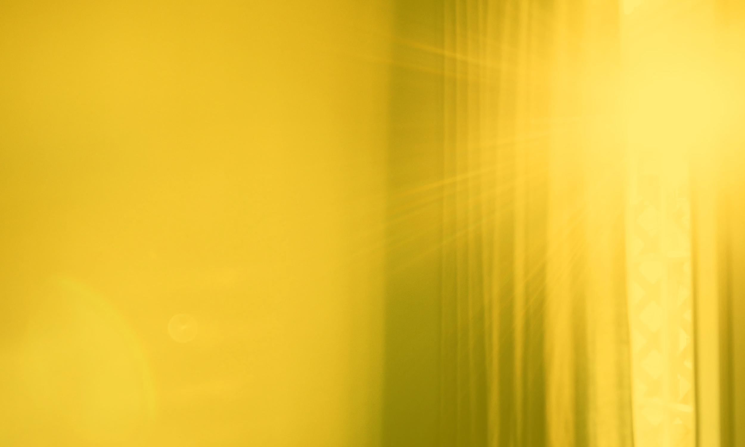 Blurred yellow surface with streaks and faint circular light reflections.