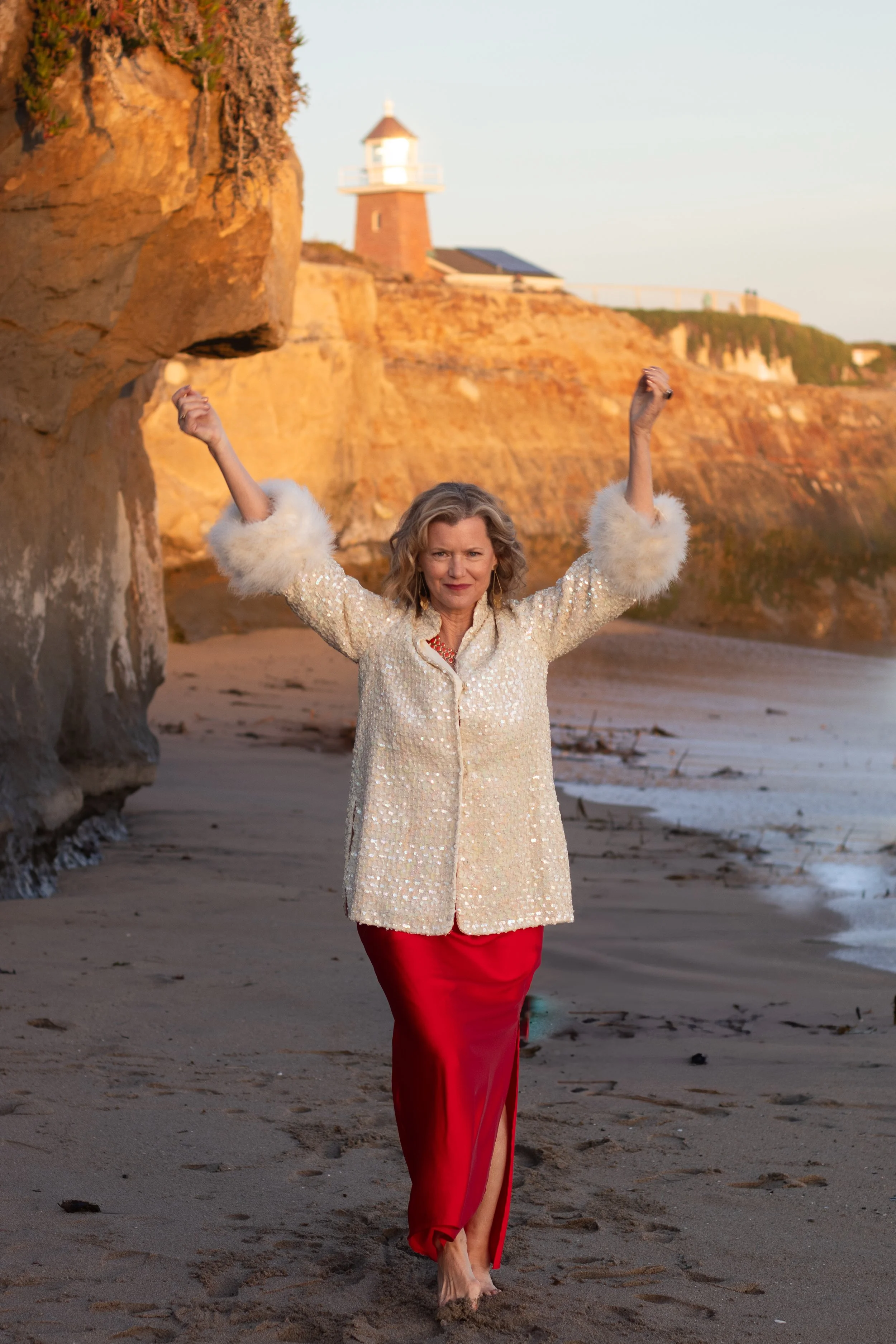 intuitive healing coach standing on beach with arms raised expressing freedom and emotional release