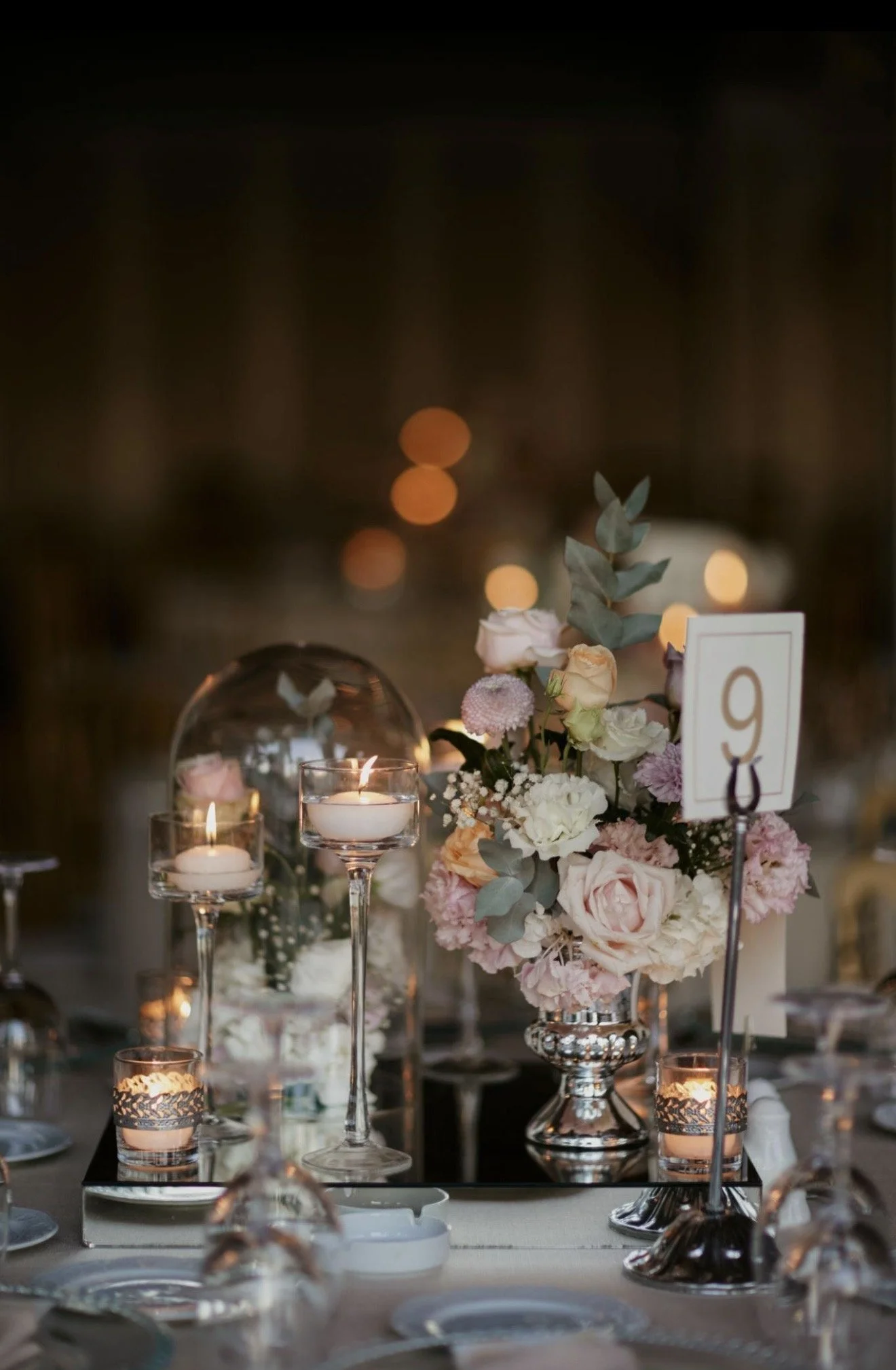 Elegant table setting with floral centerpieces, candles, and reflective glassware at a nighttime event.