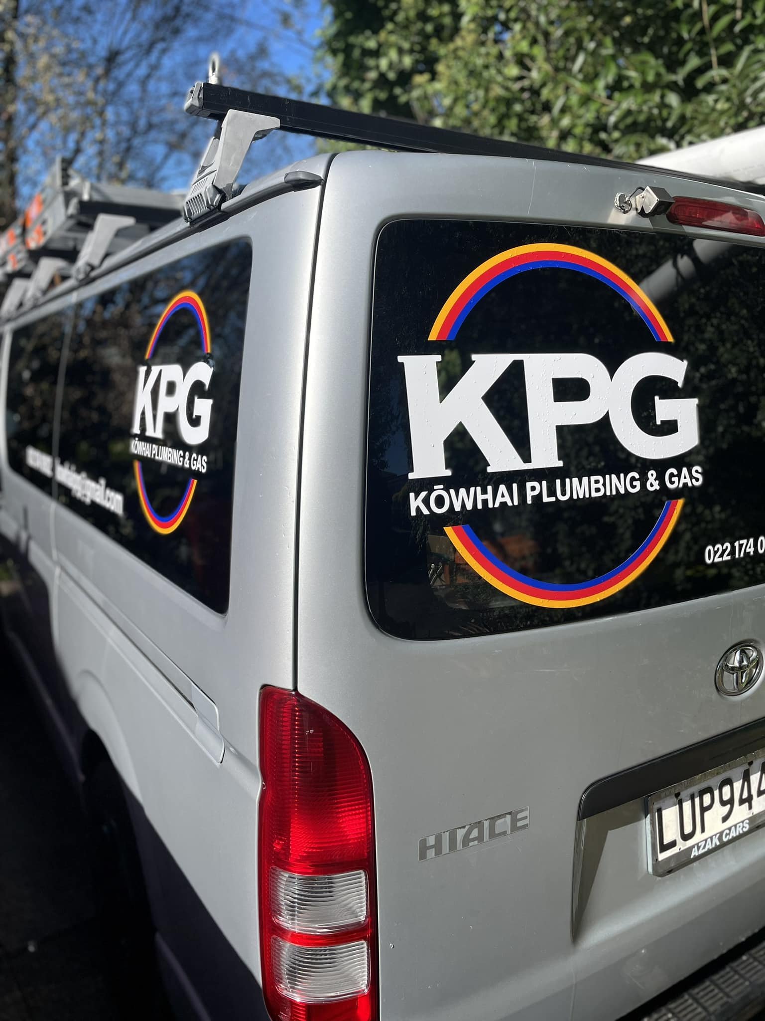 Back of a silver Toyota Hiace van with a KPG logo sticker, including a rainbow design and the text "KÖWHAI PLUMBING & GAS."