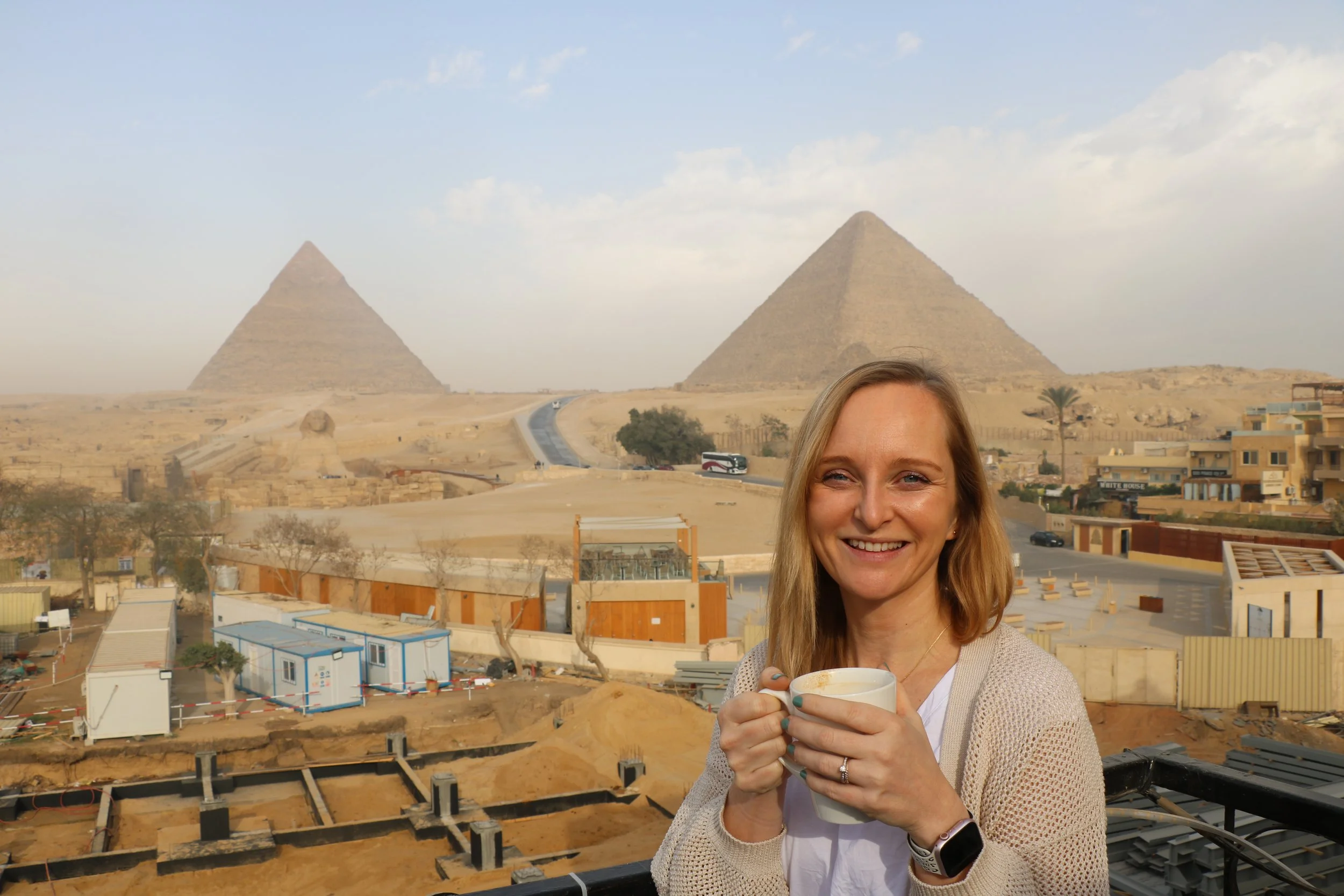 Woman smiling and holding a mug with the pyramids of Giza in the background in Egypt.